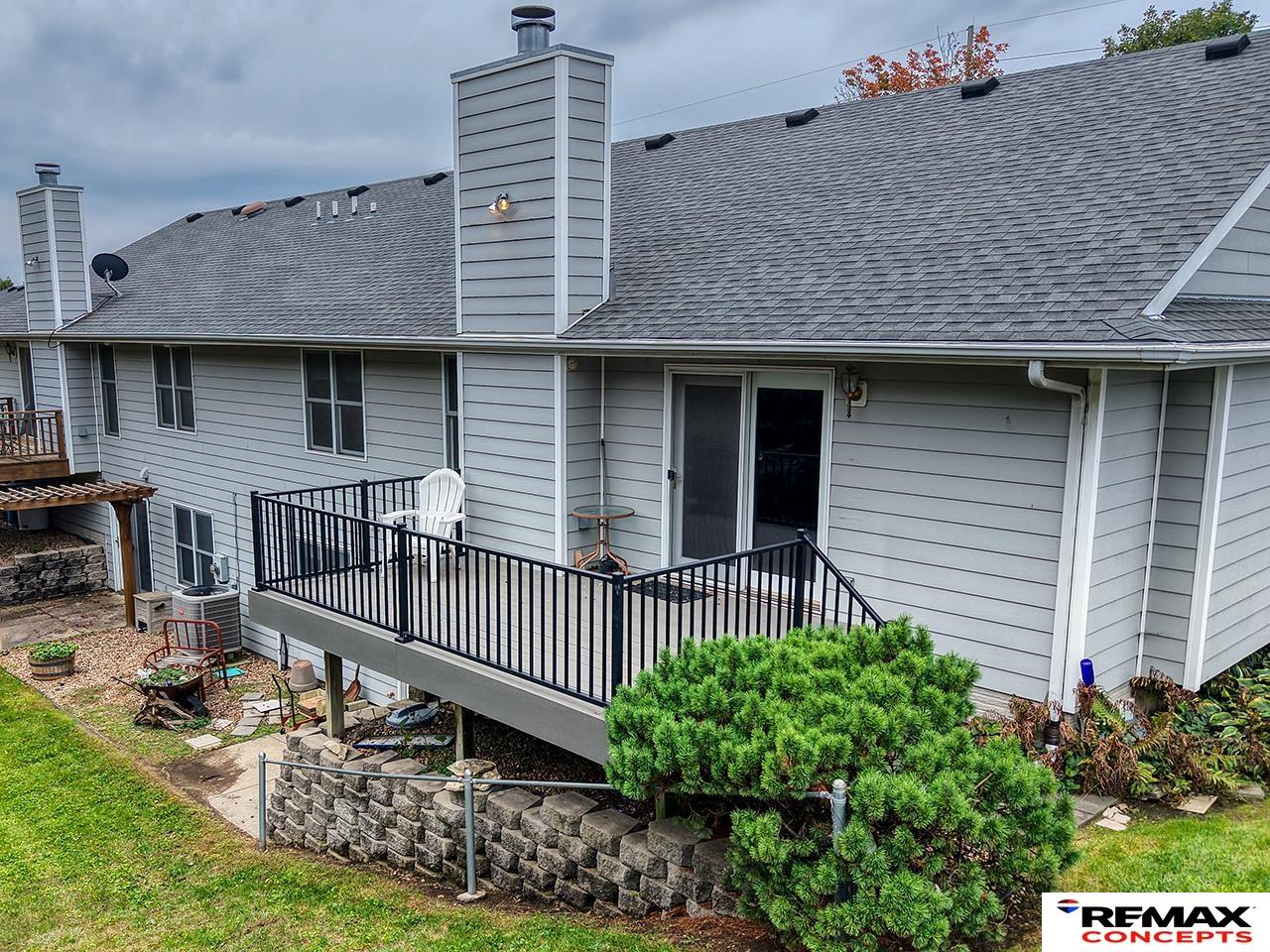 Rear of a gray-sided home with a raised deck, black railings, and a stone retaining wall.