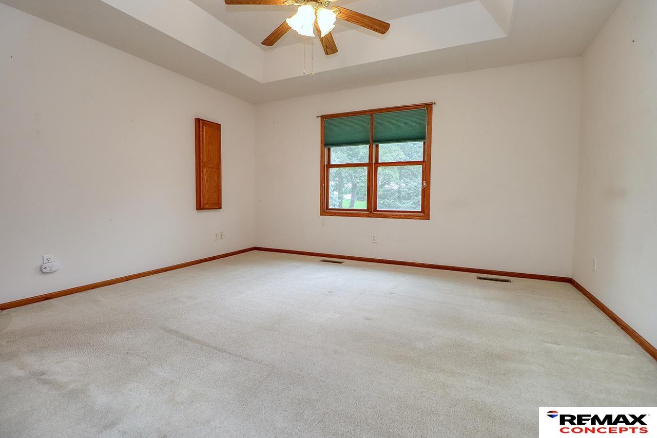 Empty carpeted bedroom with a tray ceiling, ceiling fan, and wood-trimmed window.