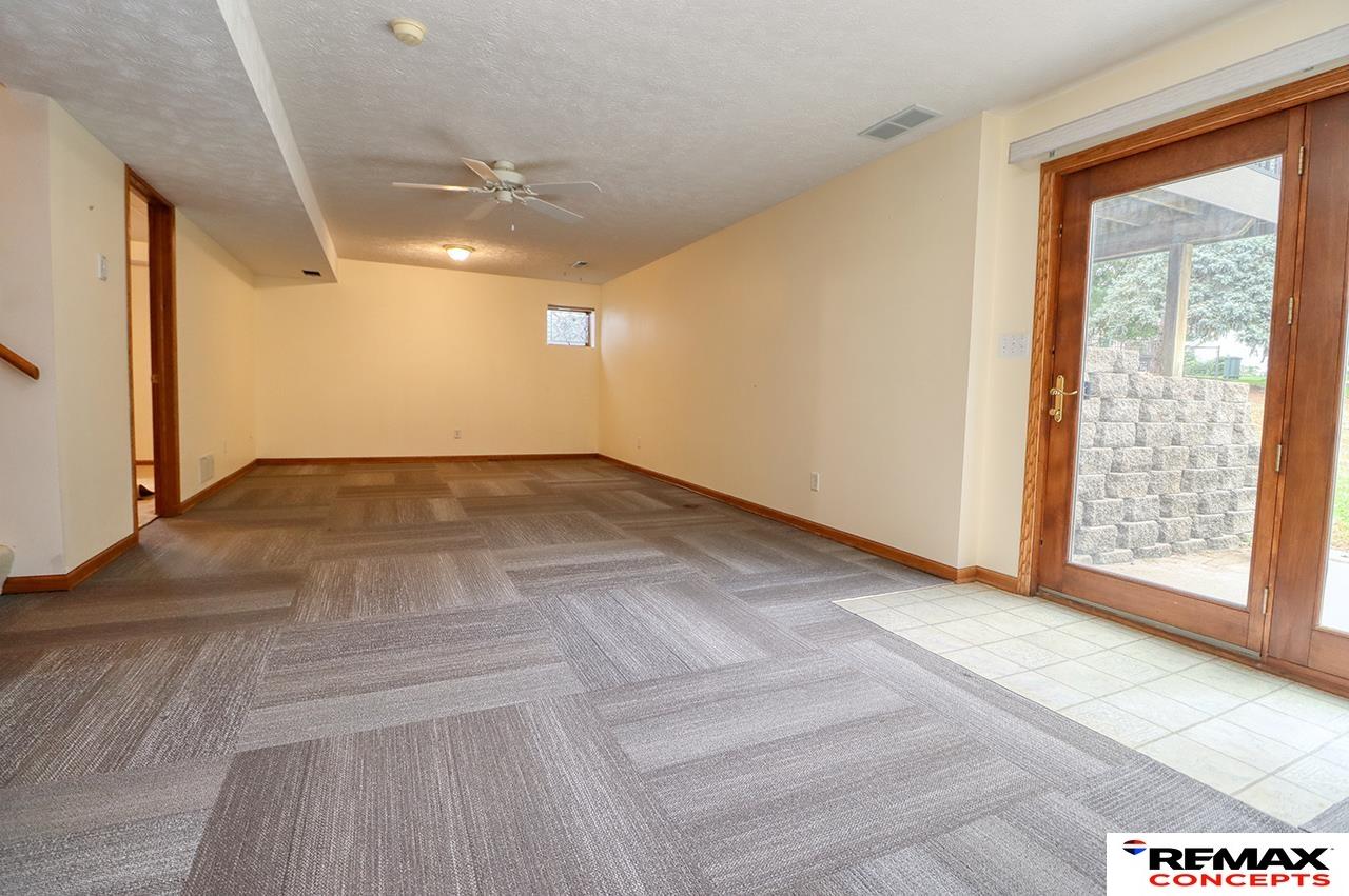 Empty carpeted living area with a ceiling fan and wood-framed glass patio door.