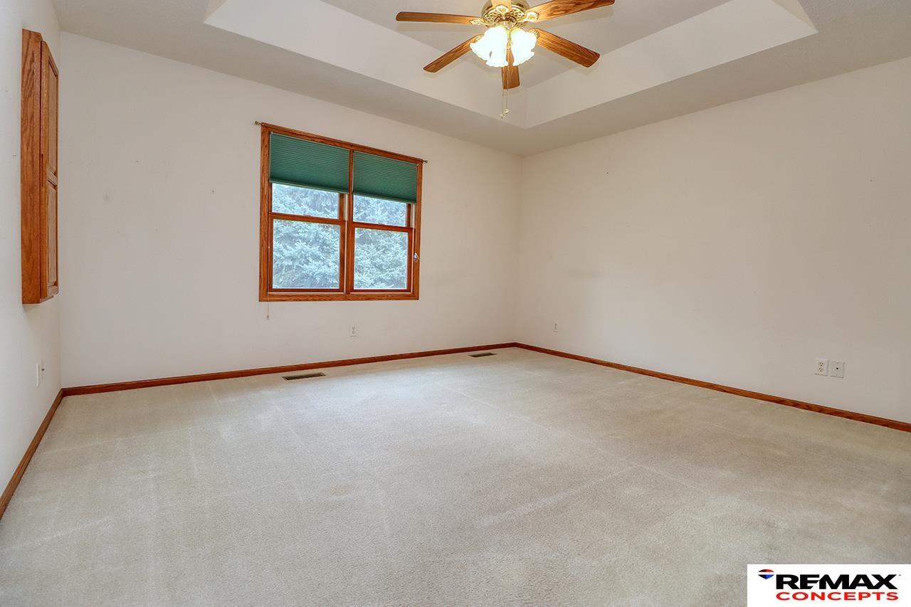 Empty bedroom with beige carpet, wood-trimmed window and green blinds, and a ceiling fan.