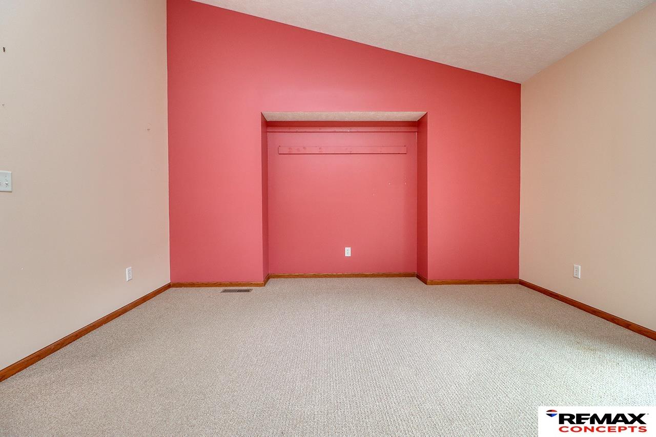 Empty bedroom with a recessed closet nook, beige carpet, and coral accent wall.