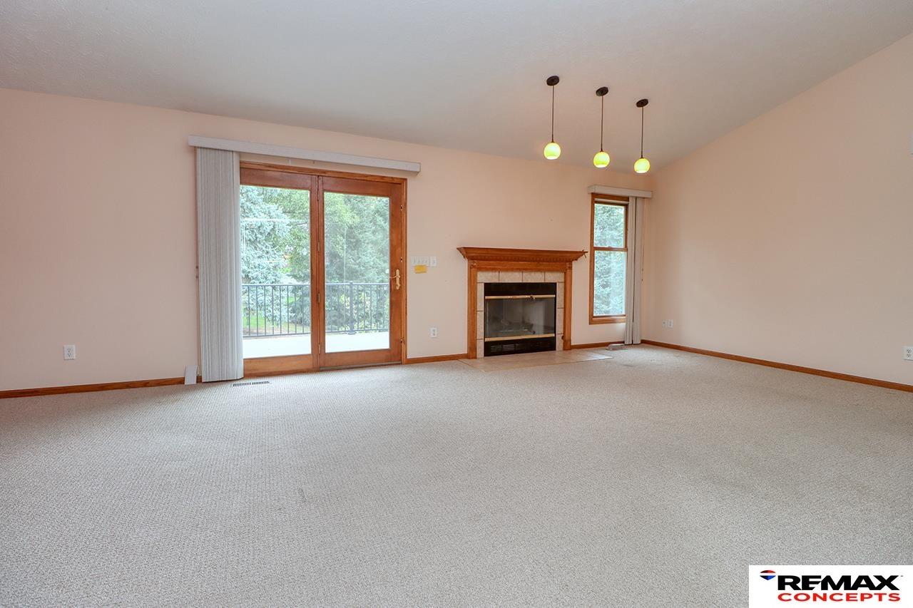 Empty living room with a gas fireplace, sliding glass door, and light carpeting.