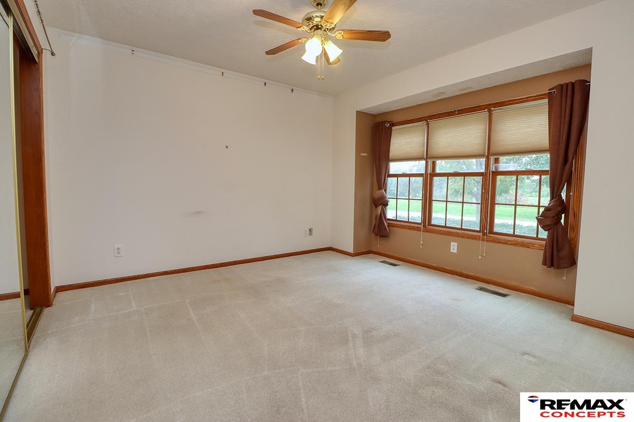 Empty carpeted room with a ceiling fan and three large curtained windows.