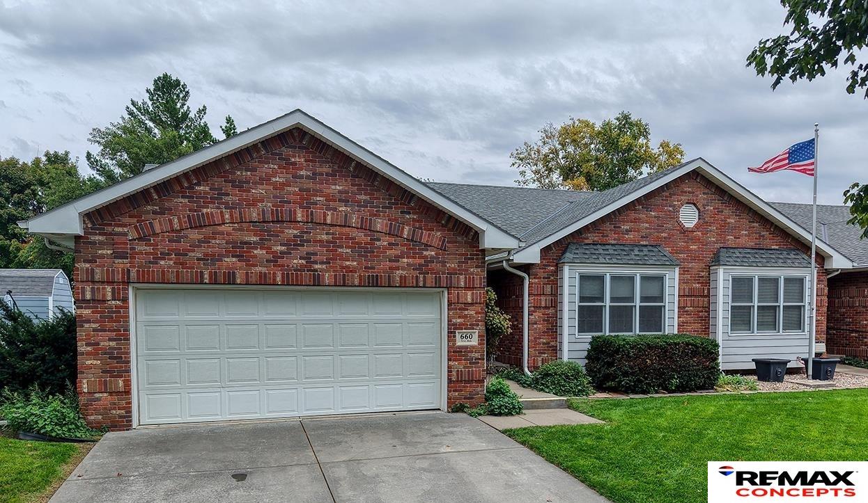 Red-brick single-story home with an attached double garage and an American flag.