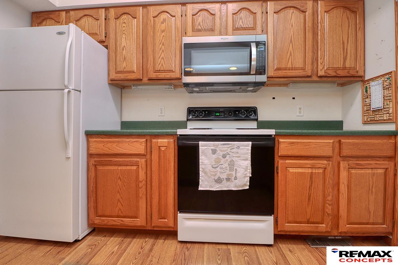 Kitchen with honey-colored wood cabinets, green countertops, white appliances, and wood flooring.