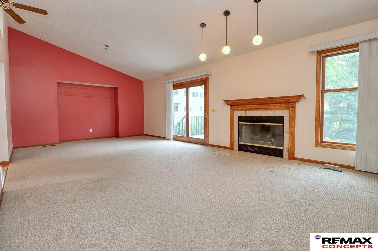 Empty living room with a wood-trimmed fireplace, red accent wall, and sliding glass doors.