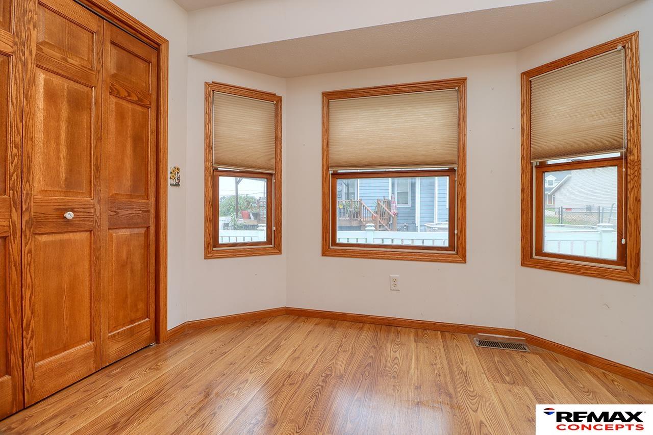 Empty room with three windows, wood-look flooring, and large wooden closet doors.