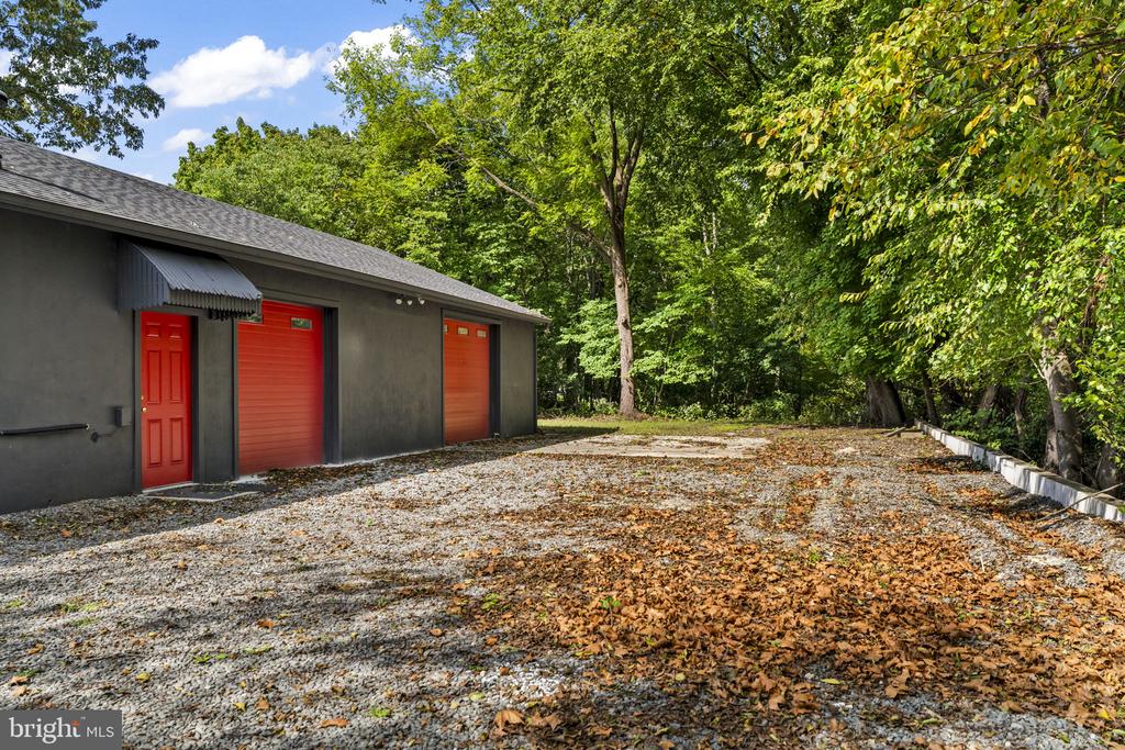 Garage with three red doors beside a leaf-strewn gravel driveway and mature trees.