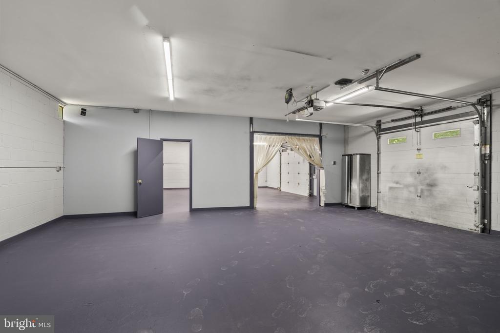 Vacant garage with a wide floor, overhead door, and curtained opening to a second garage area.