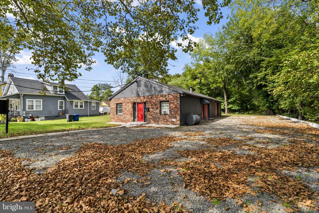Single-story brick building with a bright red entrance beside a broad gravel parking area.