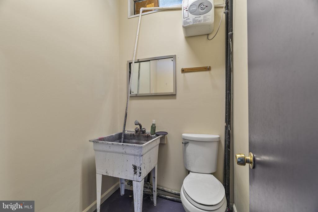 Utility bathroom with a toilet, deep sink, wall-mounted water heater, and small mirror.