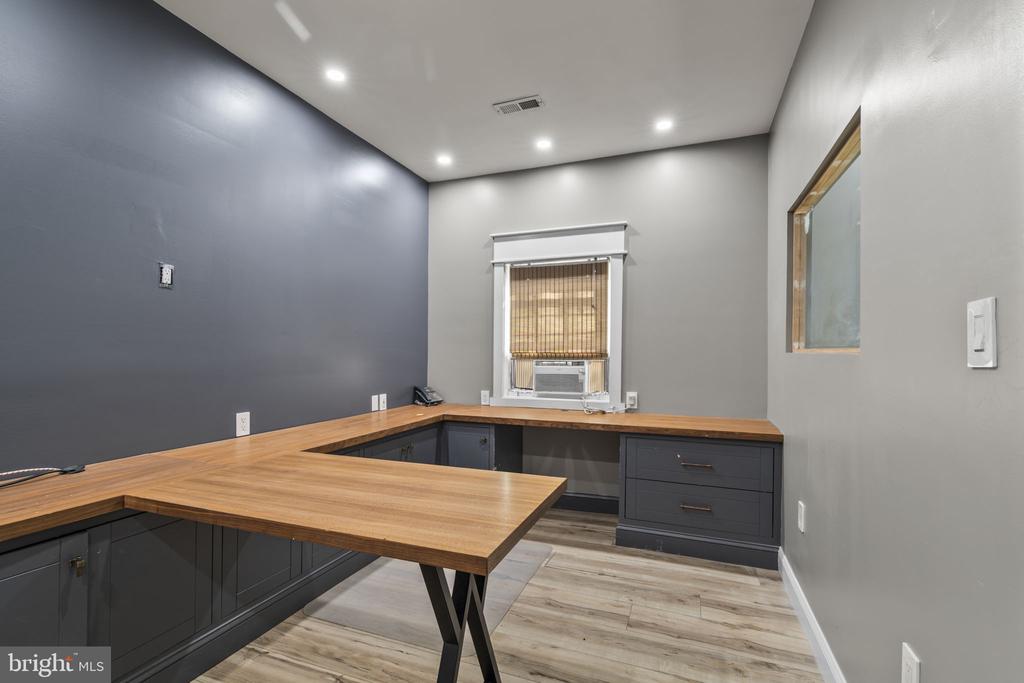 Empty office with charcoal built-in cabinets, broad wood counters, and a window air conditioner.