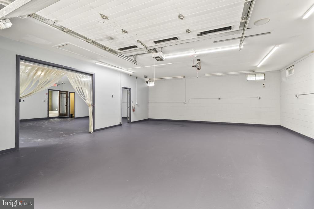 Empty garage with a wide overhead door, gray floor, and curtained opening to adjoining room.