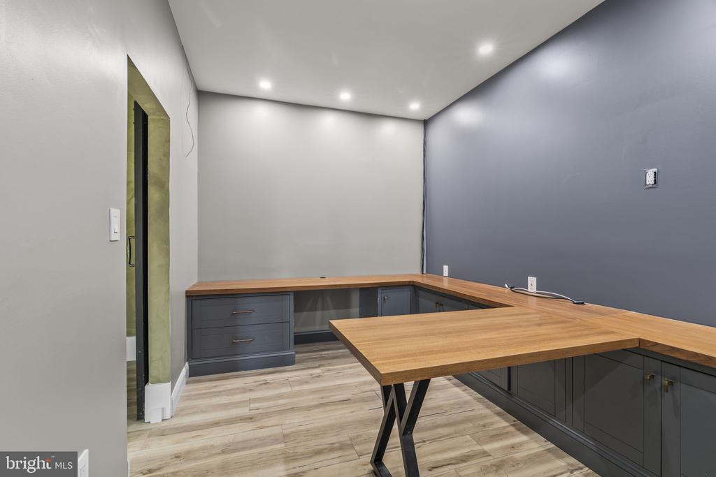 Office with L-shaped wood countertops, dark built-in cabinets, and light wood-look flooring.
