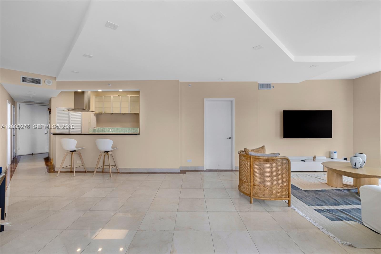 Open-plan living room with a breakfast bar, wicker chair, and wall-mounted television.