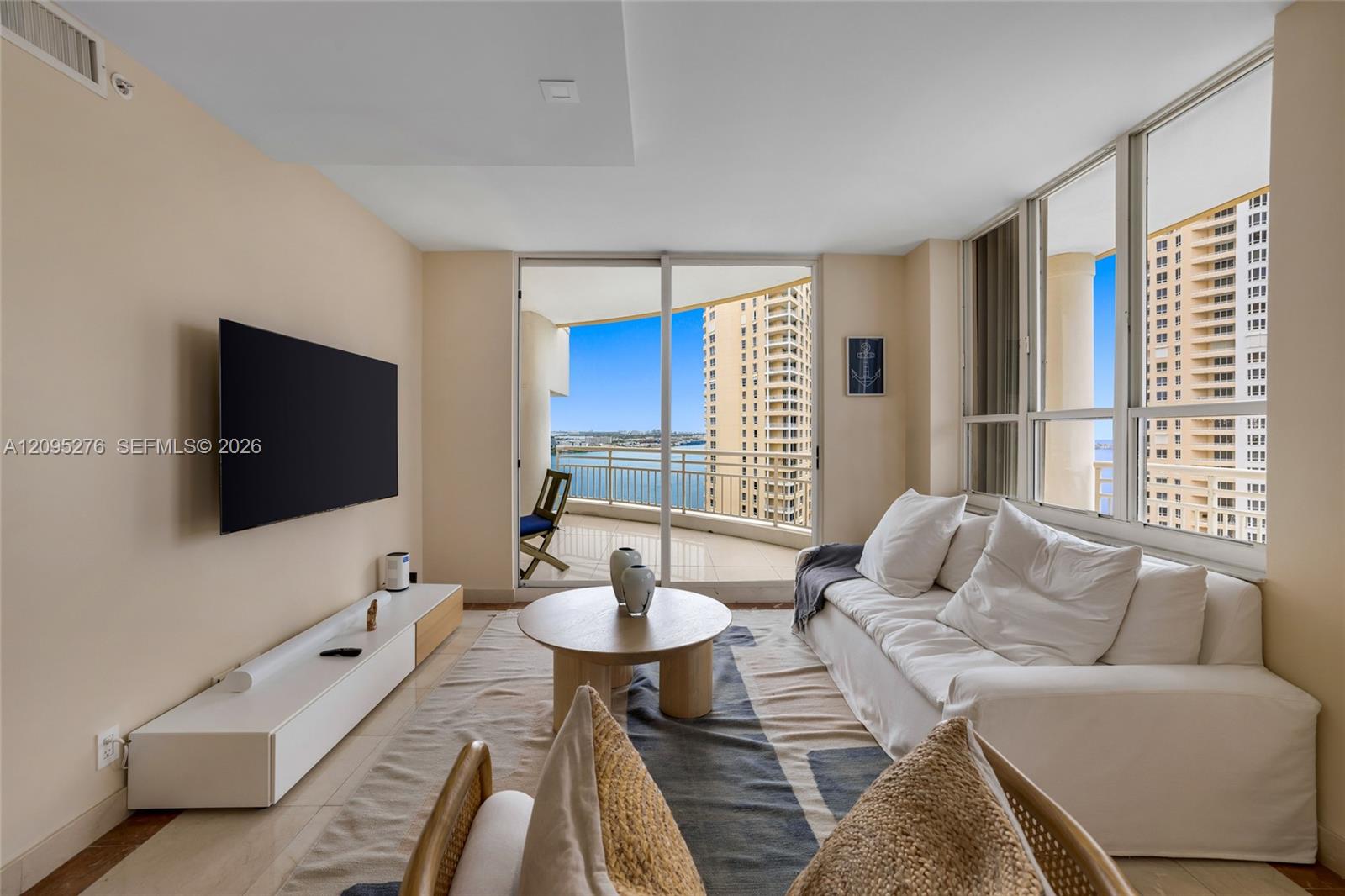 Condo living room with a white sectional, balcony, and water views between high-rise buildings.