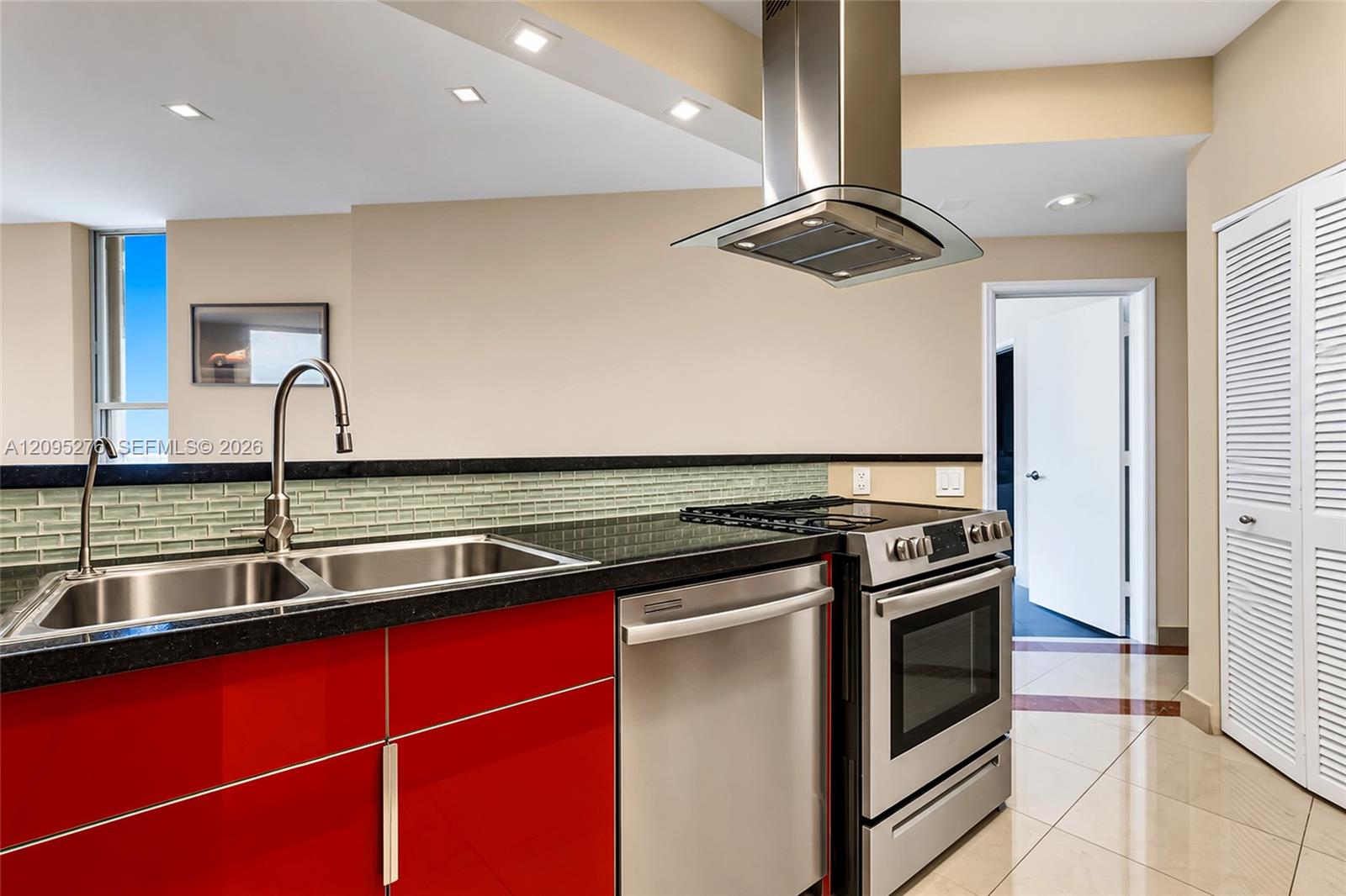 Modern kitchen with glossy red cabinets, black countertops, green glass-tile backsplash, and stainless-steel appliances.