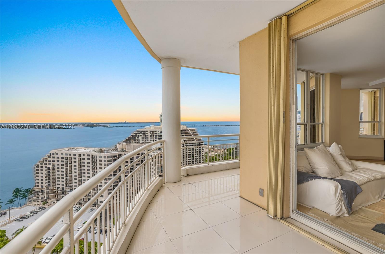 Curved high-rise balcony overlooking the bay, with a tiled floor and sliding doors to a bedroom.