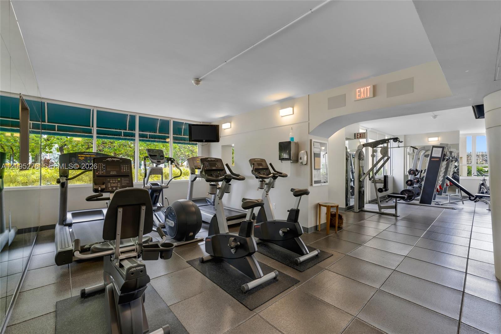 Building fitness center with cardio machines, weight equipment, and large windows.