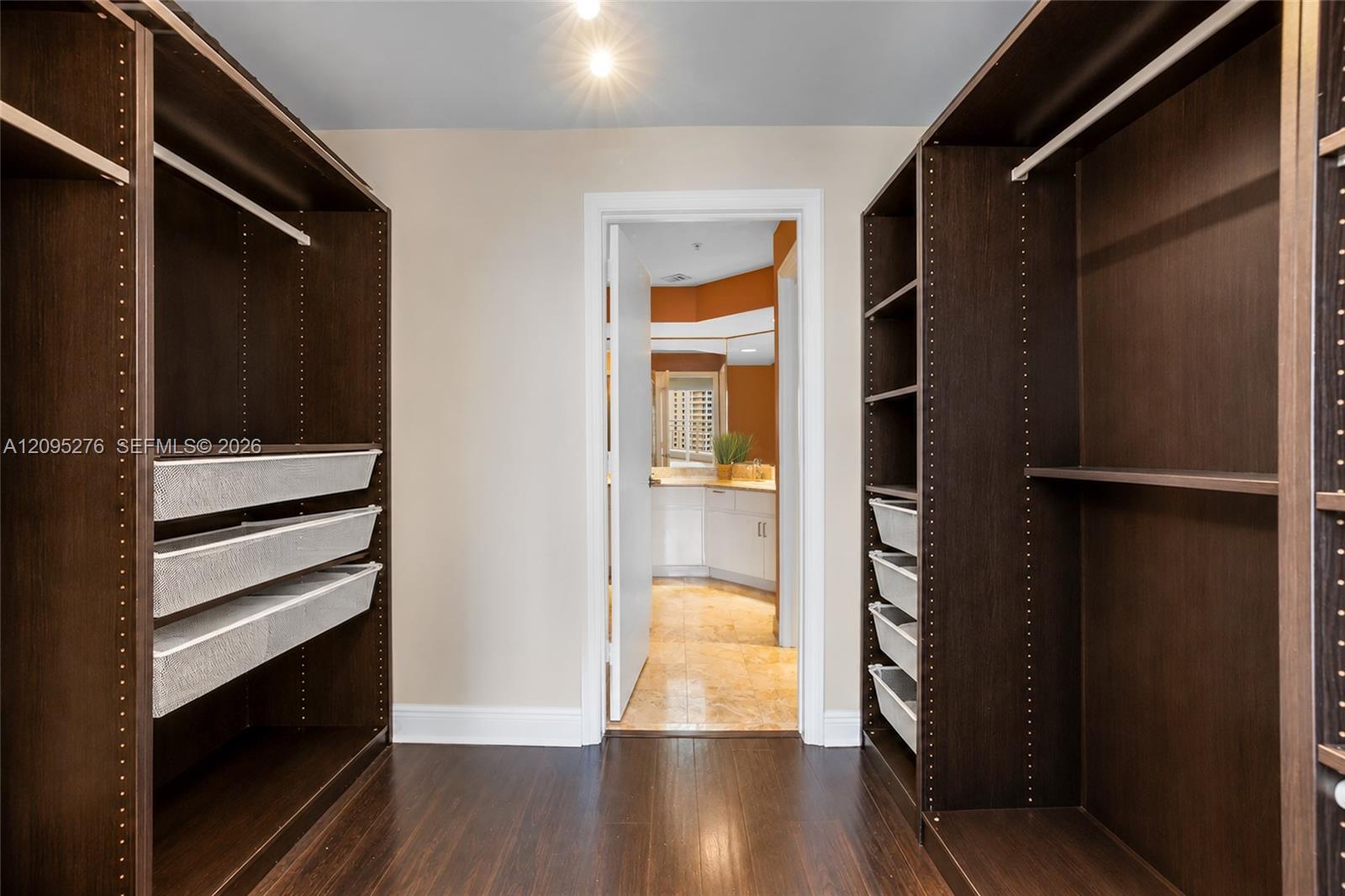 Walk-in closet with dark wood built-ins and mesh drawers, opening to a bathroom vanity.