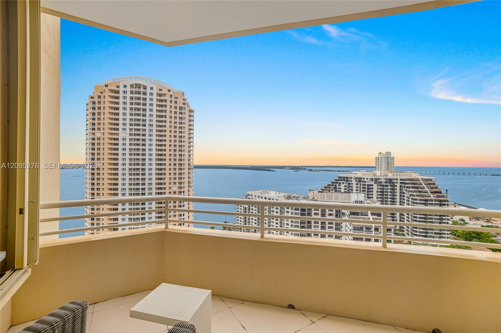 High-rise balcony overlooking Biscayne Bay, neighboring towers, and a distant bridge at sunset.