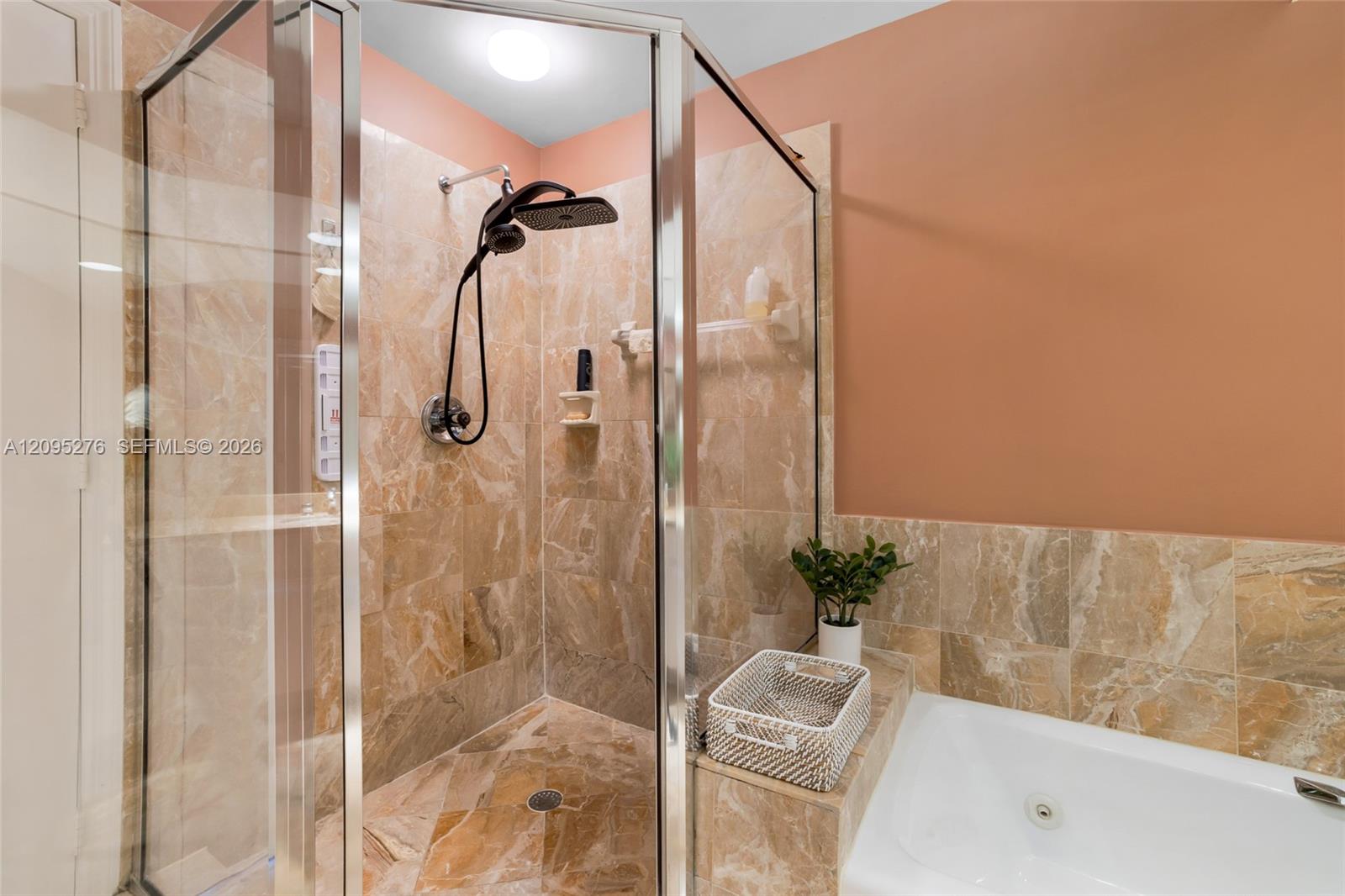 Bathroom with a glass-enclosed marble-look shower, black rainfall showerhead, and white bathtub.