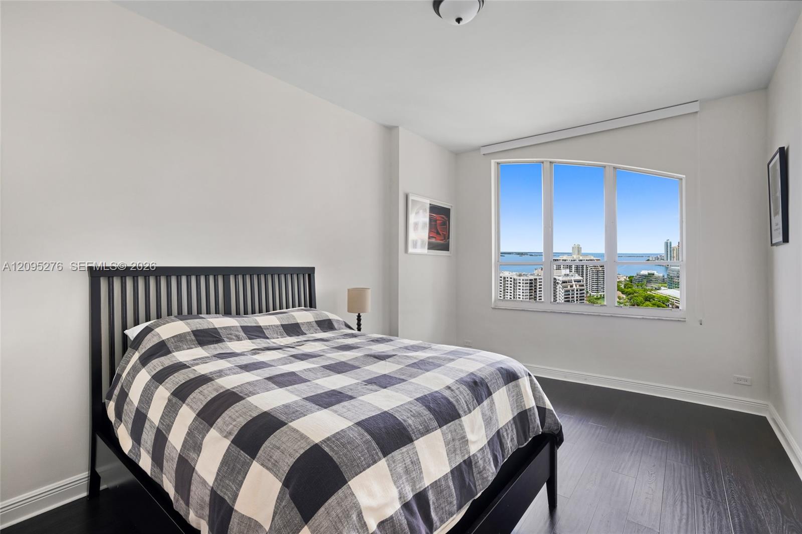 Bedroom with checkered bedding and a large window overlooking the city and water.