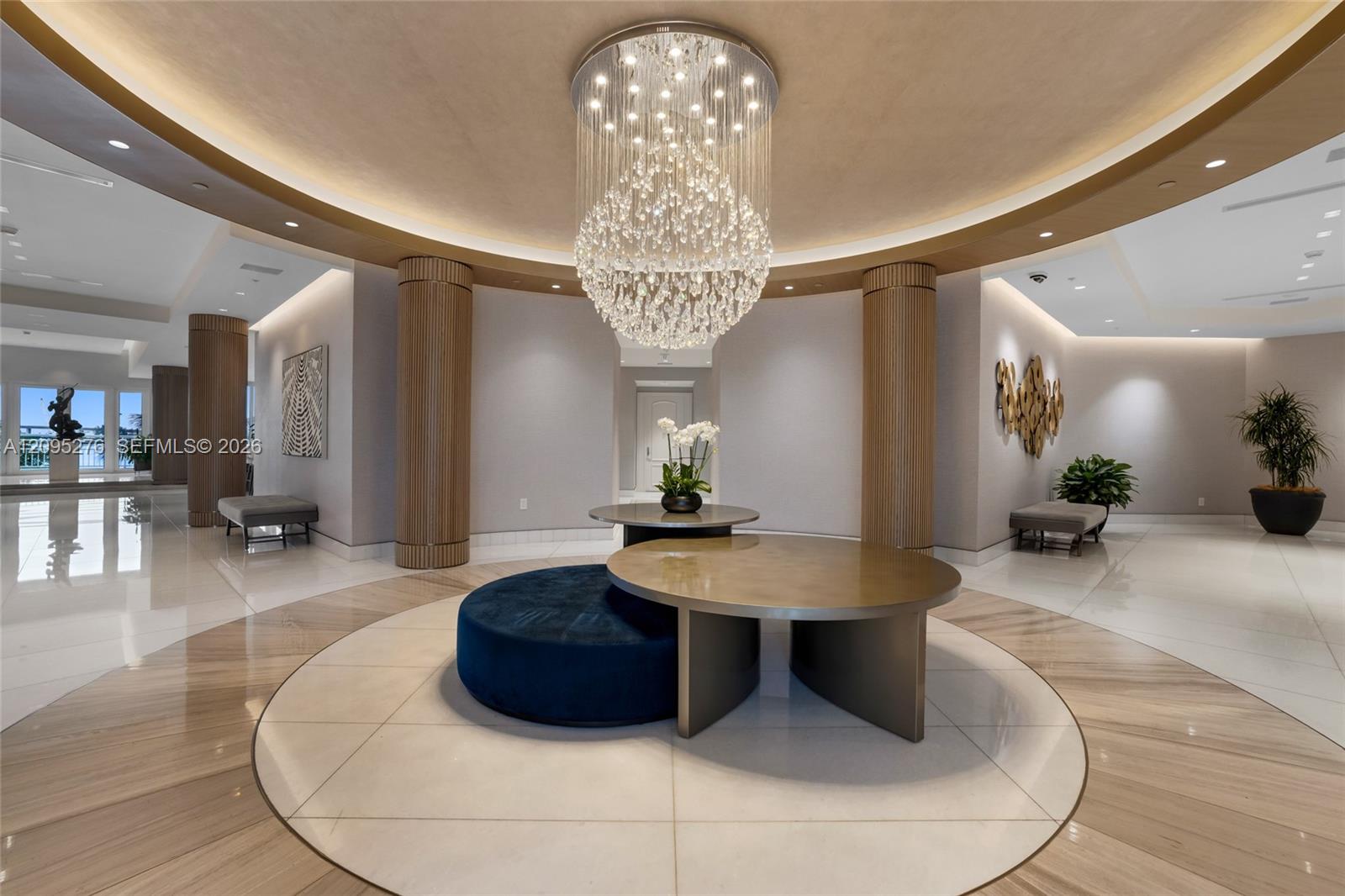 Residential lobby with a large crystal chandelier, fluted columns, and circular blue lounge seating.