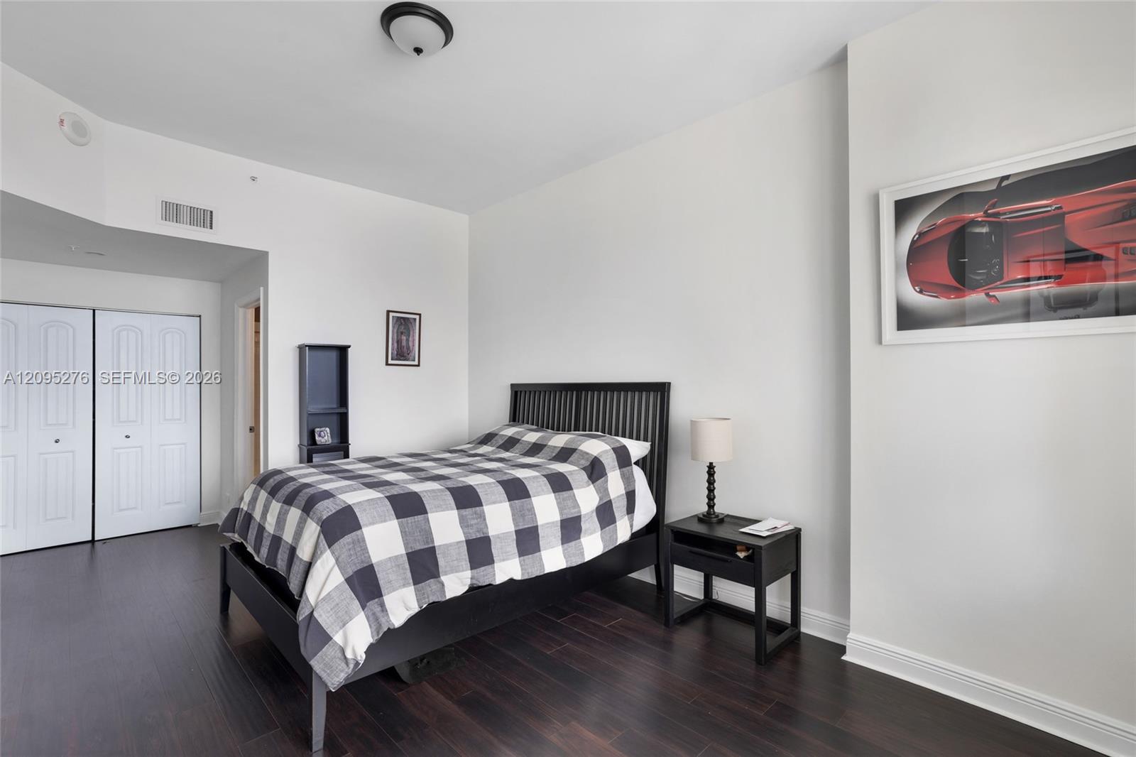 Bedroom with checkered bedding, dark wood floors, and framed red sports car artwork.