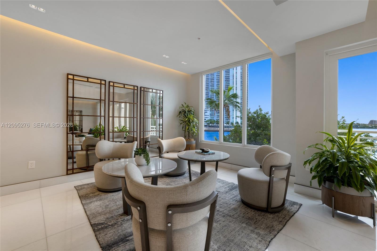 Living room with curved chairs and floor-to-ceiling windows overlooking water and high-rise buildings.