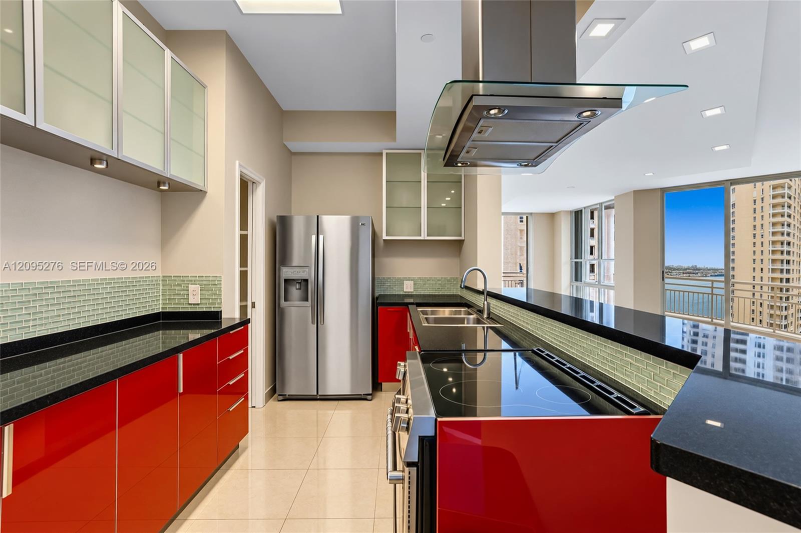 Modern kitchen with glossy red cabinets, black countertops, and windows overlooking water.