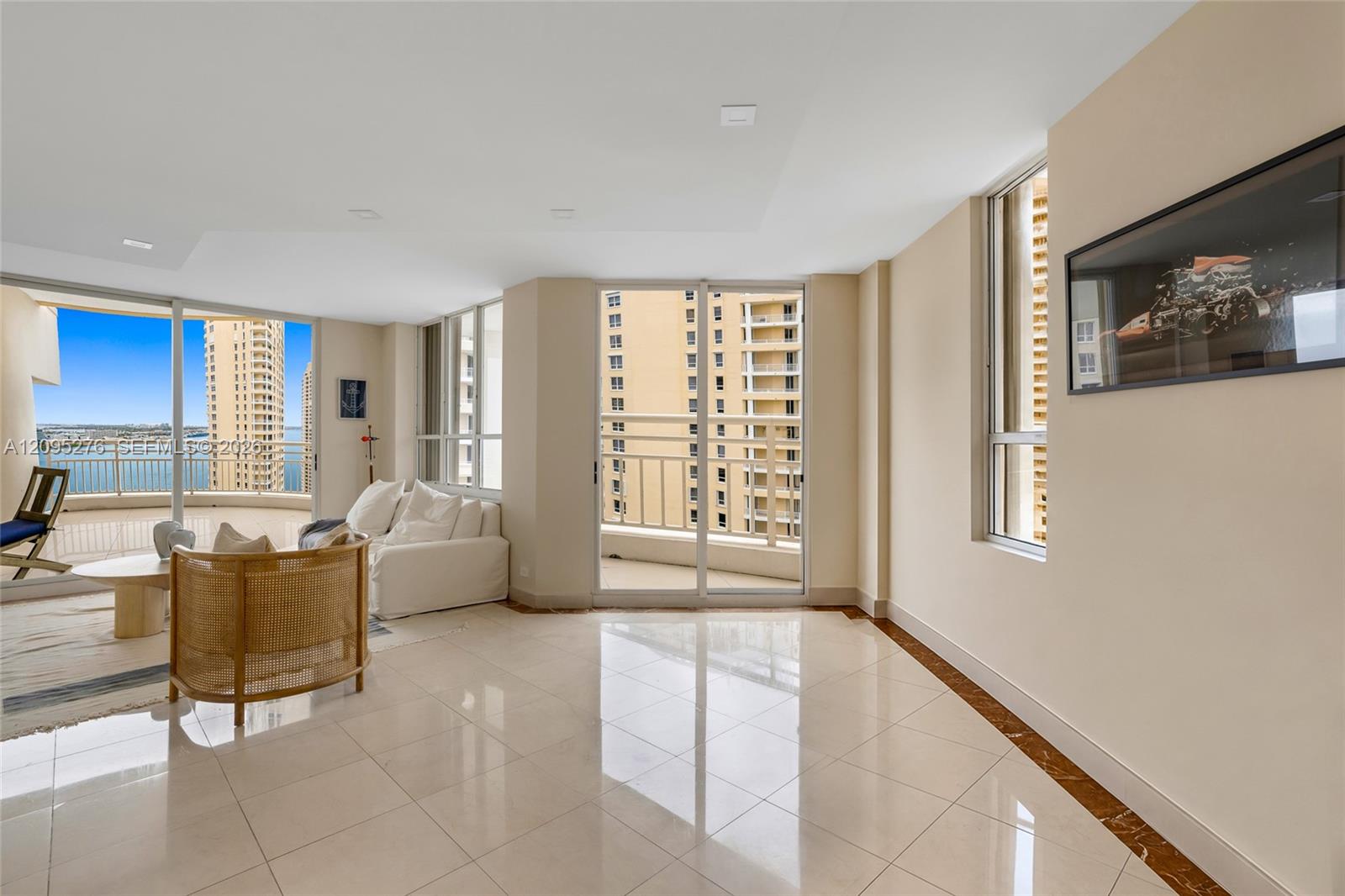 Condo living room with floor-to-ceiling windows, a balcony, and water and high-rise views.
