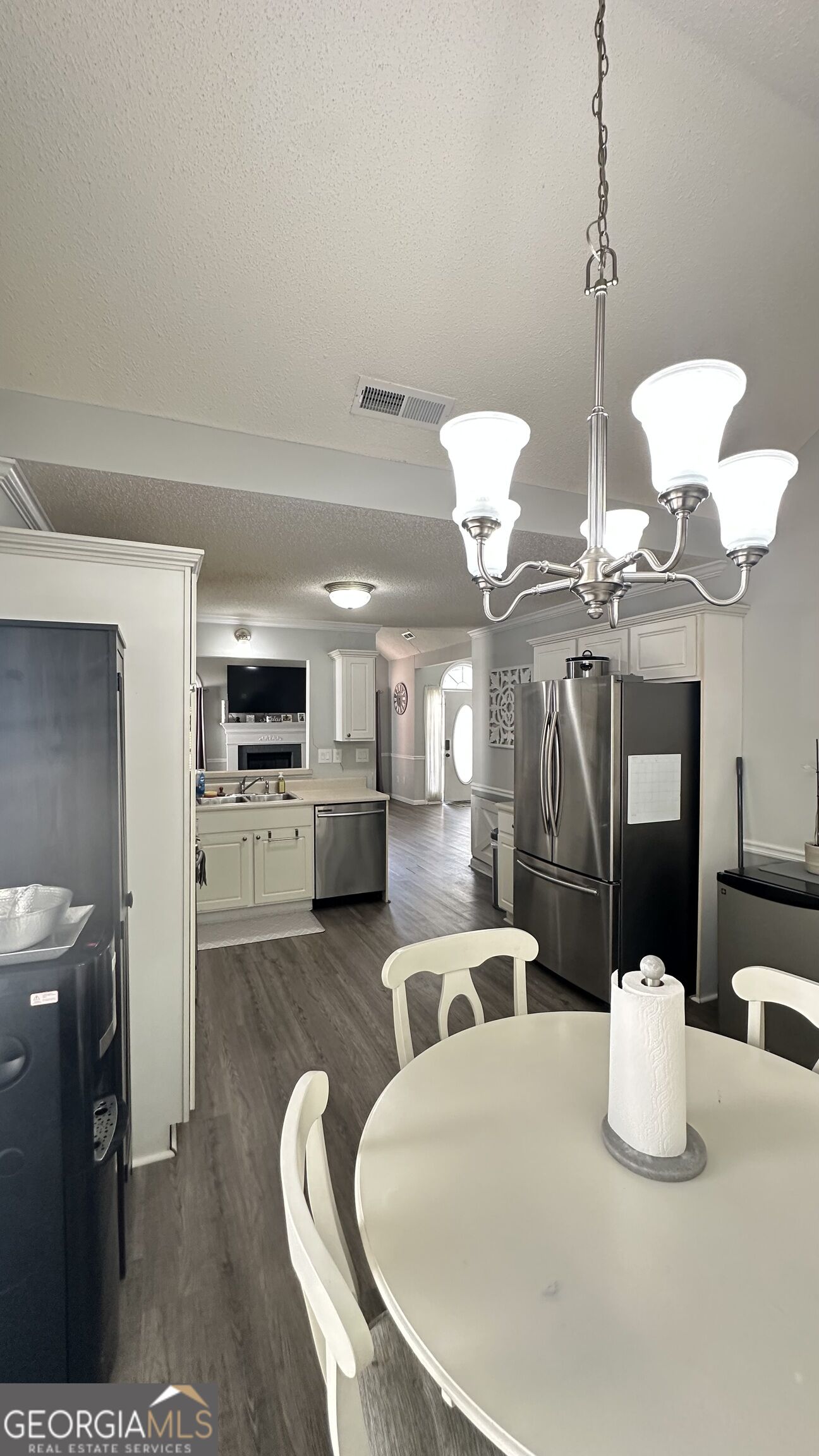 Open kitchen and dining area with white cabinets, stainless steel appliances, and a round table beneath a chandelier.
