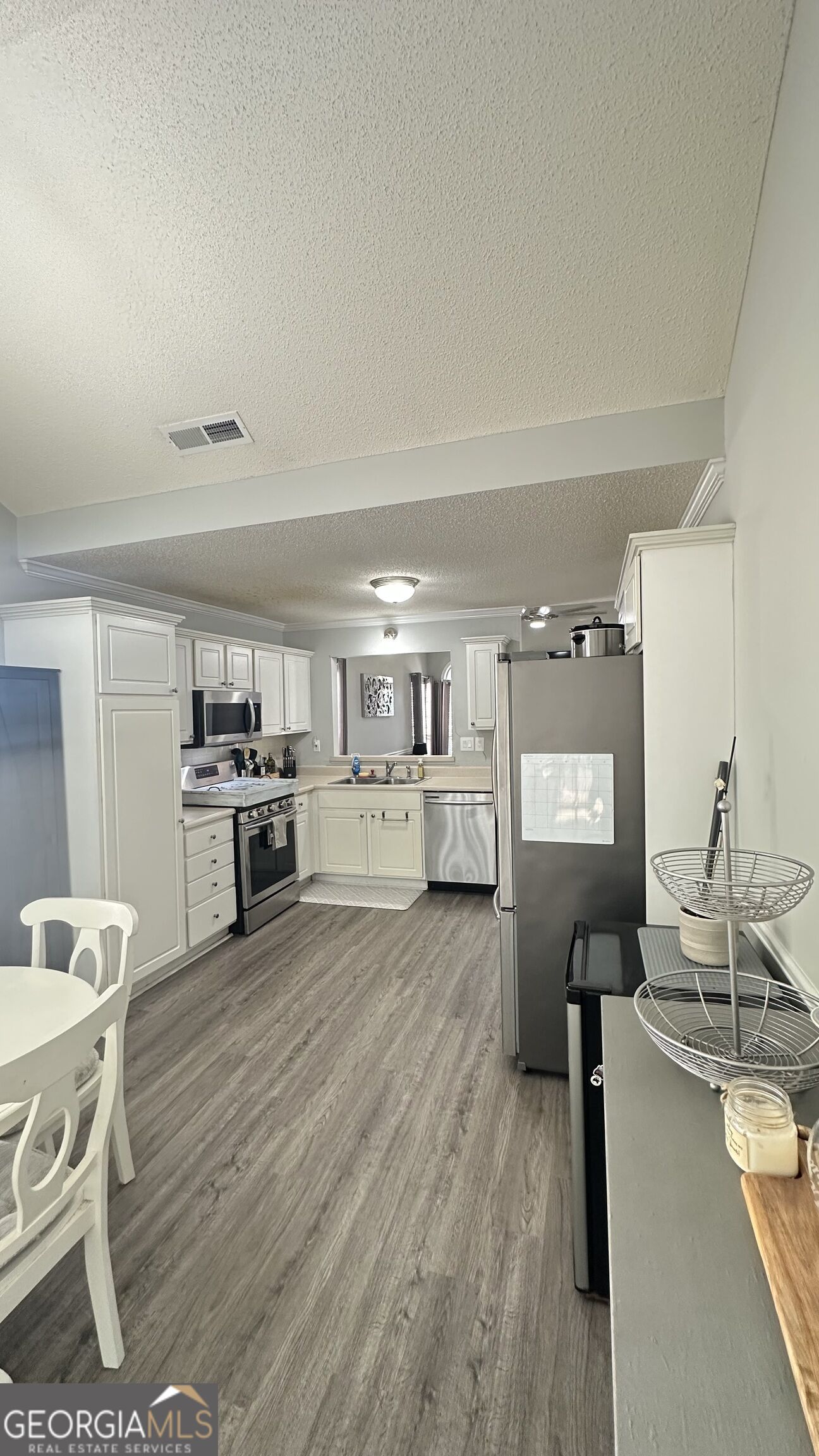 Kitchen with white cabinets, stainless steel appliances, and gray wood-look flooring.