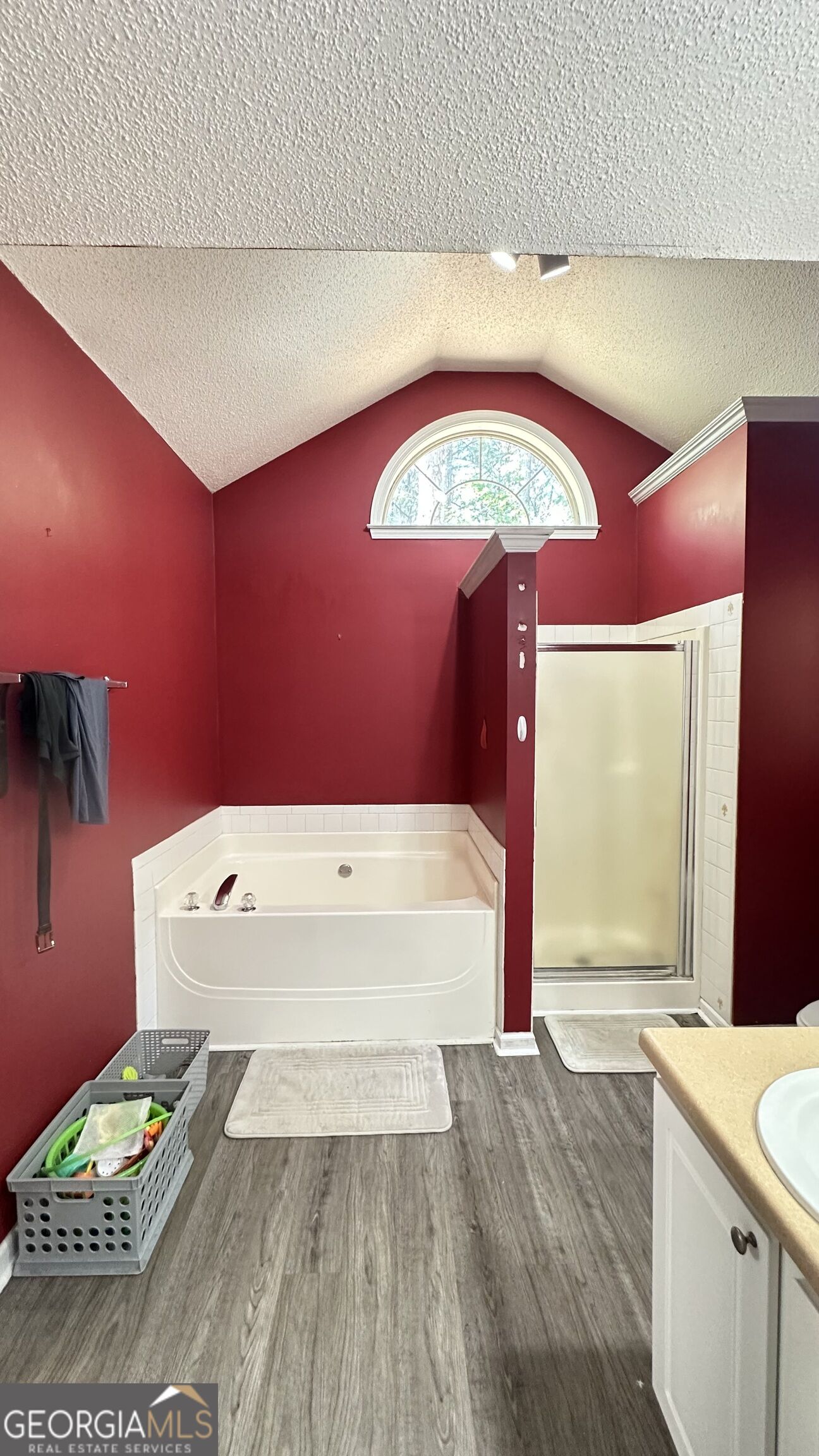 Bathroom with a white soaking tub beneath an arched window and a glass-enclosed shower.
