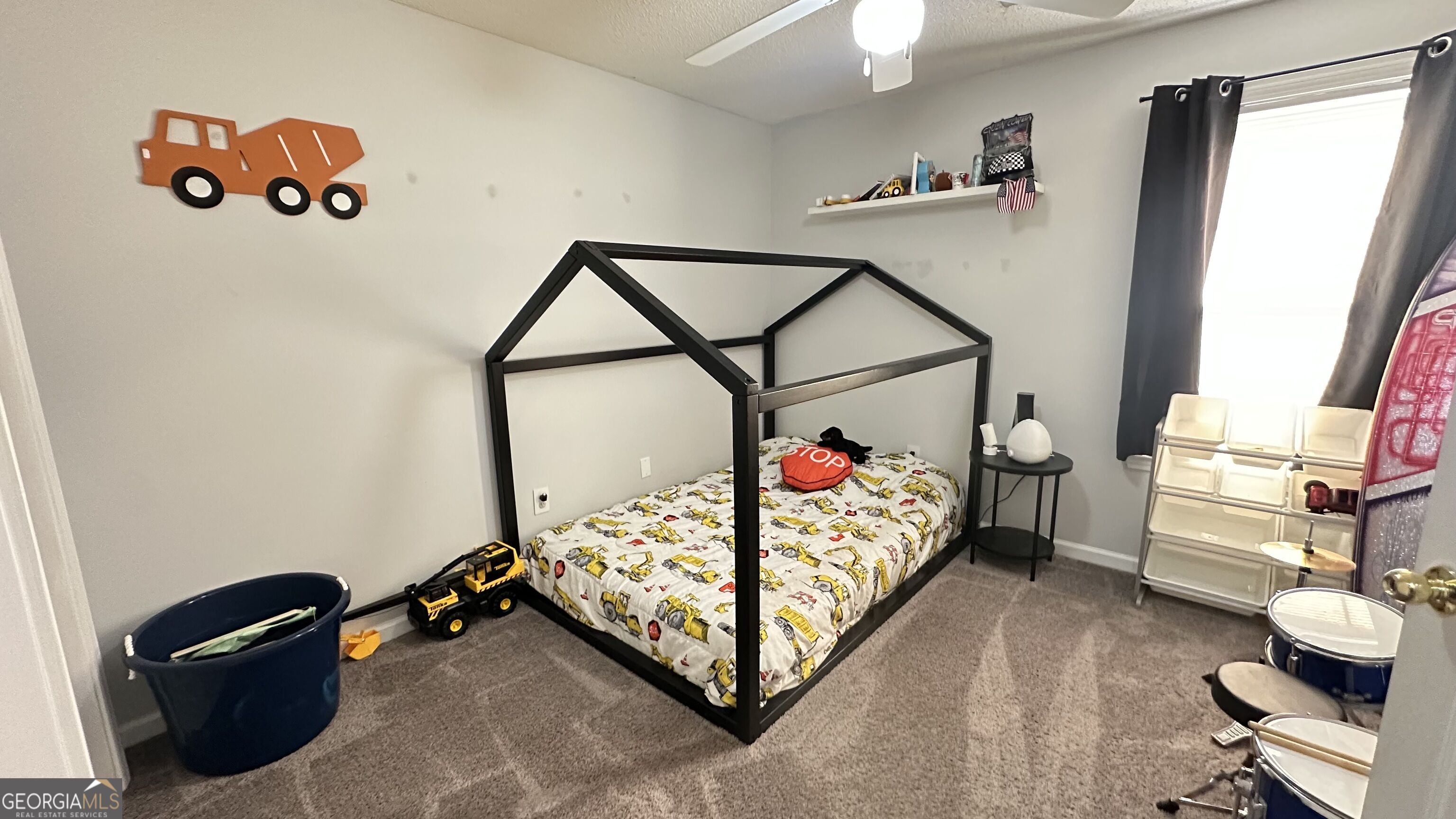 Child’s bedroom with a black house-frame bed, construction-vehicle bedding, and truck-themed wall decor.