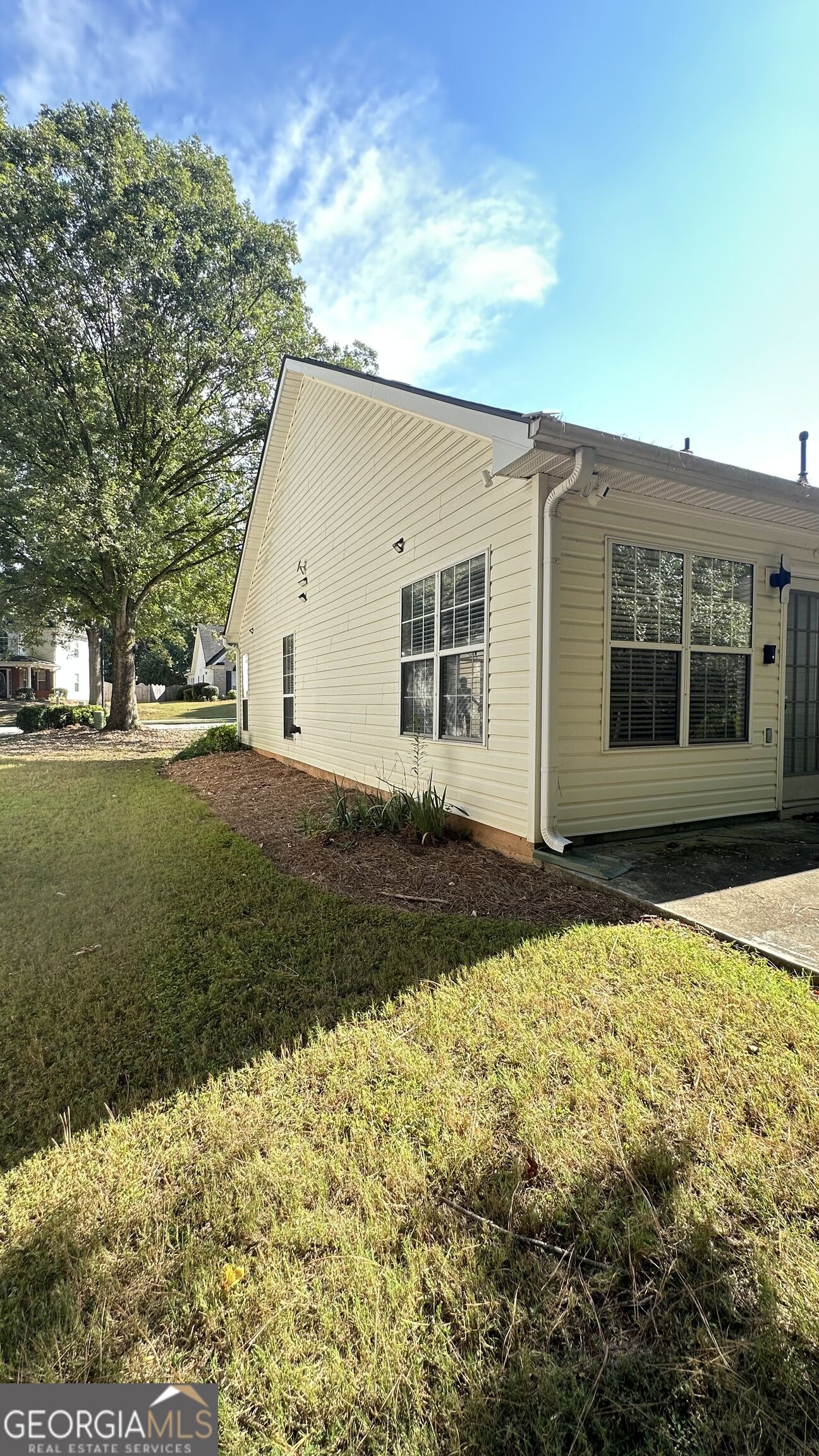 Side of a light-colored house beside a grassy yard and mature tree.