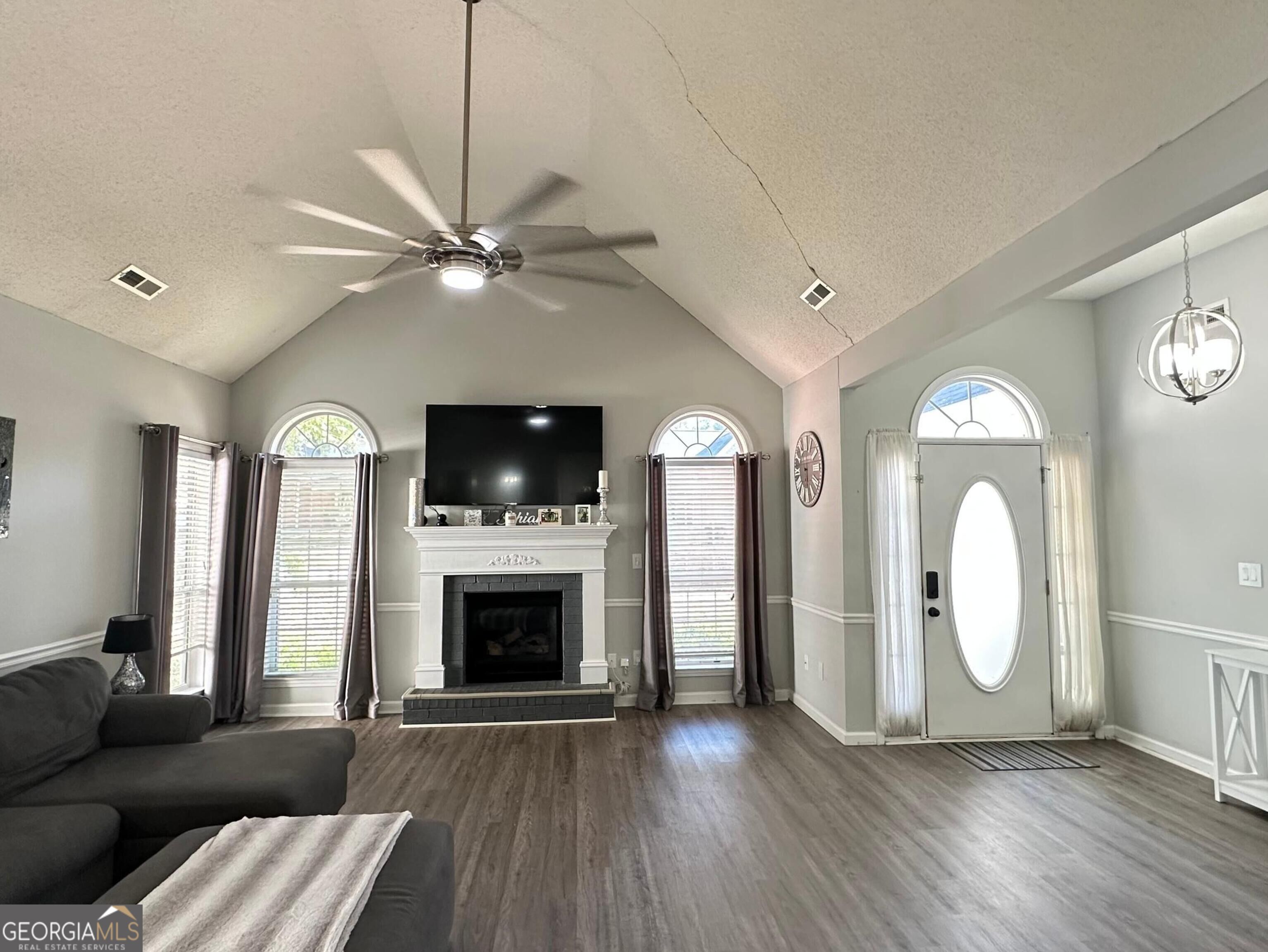 Living room with vaulted ceiling, white fireplace, arched windows, and oval-glass front door.