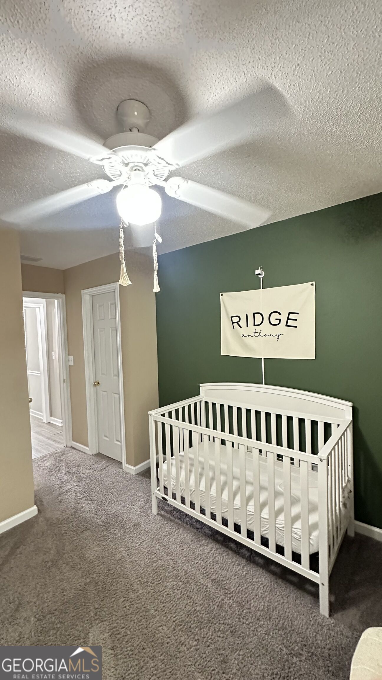 Nursery with a white crib, dark green accent wall, and ceiling fan.
