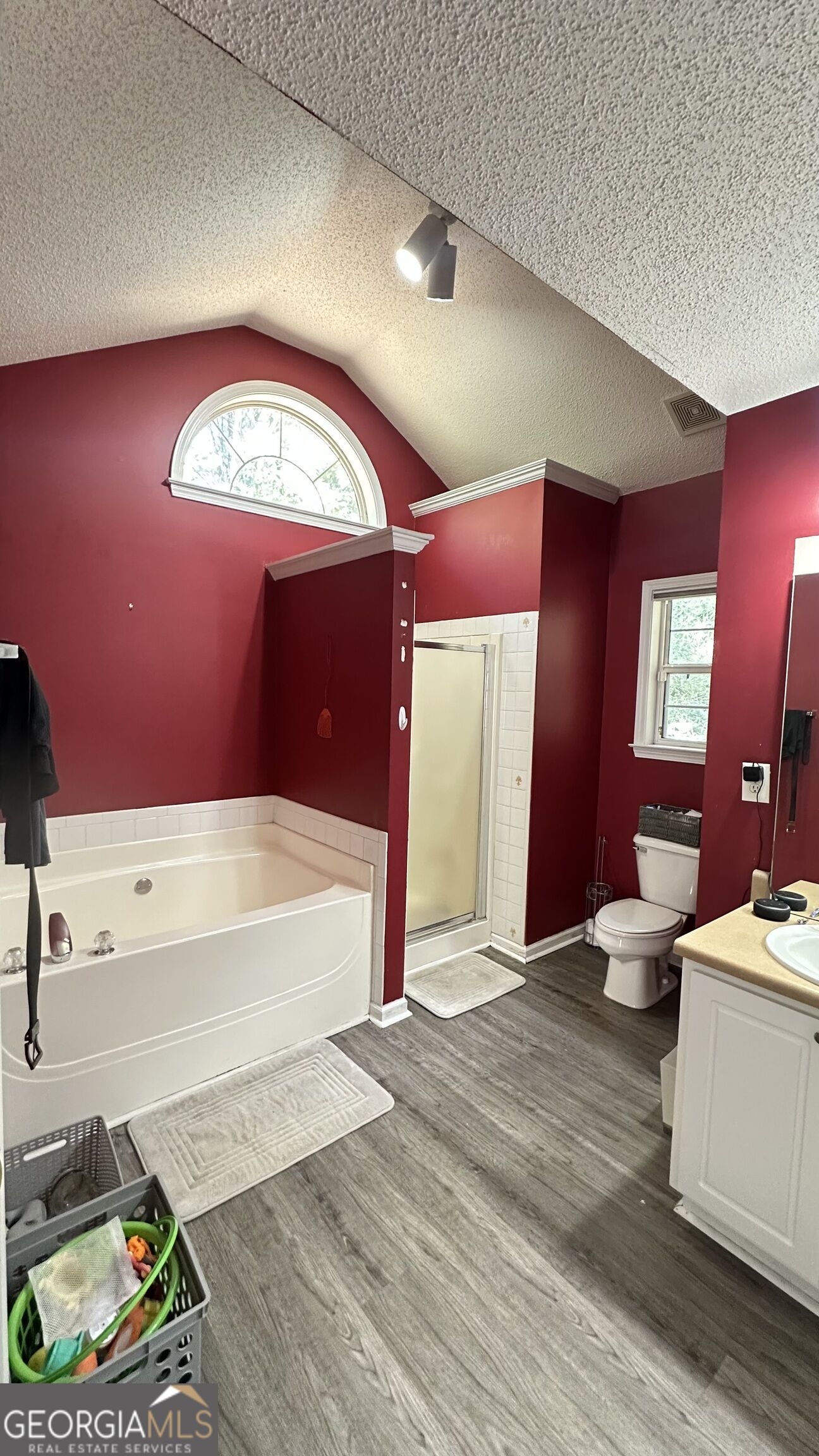 Bathroom with a soaking tub beneath an arched window and a separate shower.