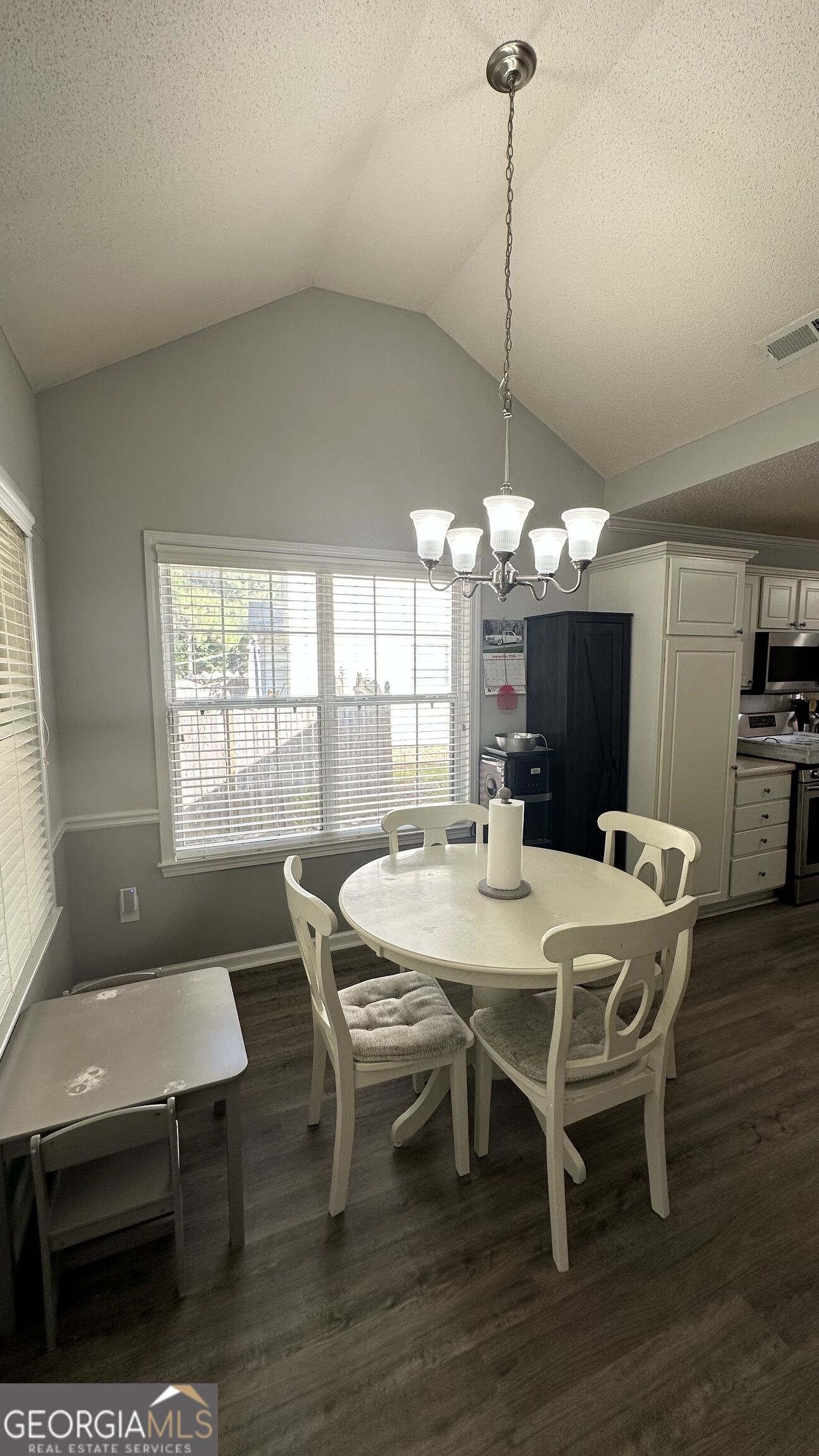 Dining area with a round white table, four chairs, and a chandelier beside the kitchen.