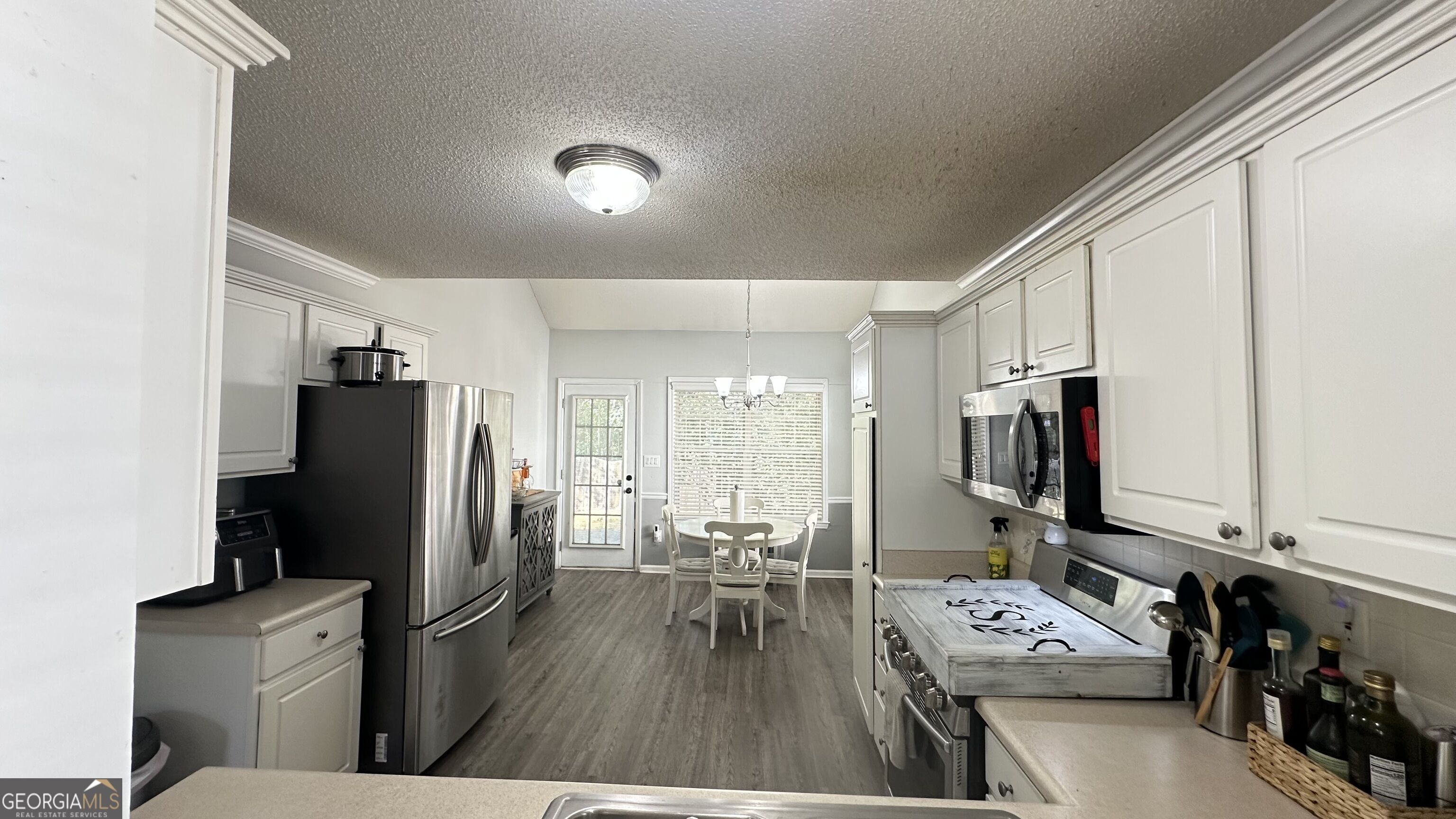 Kitchen with white cabinets and stainless steel appliances opening onto a dining area.