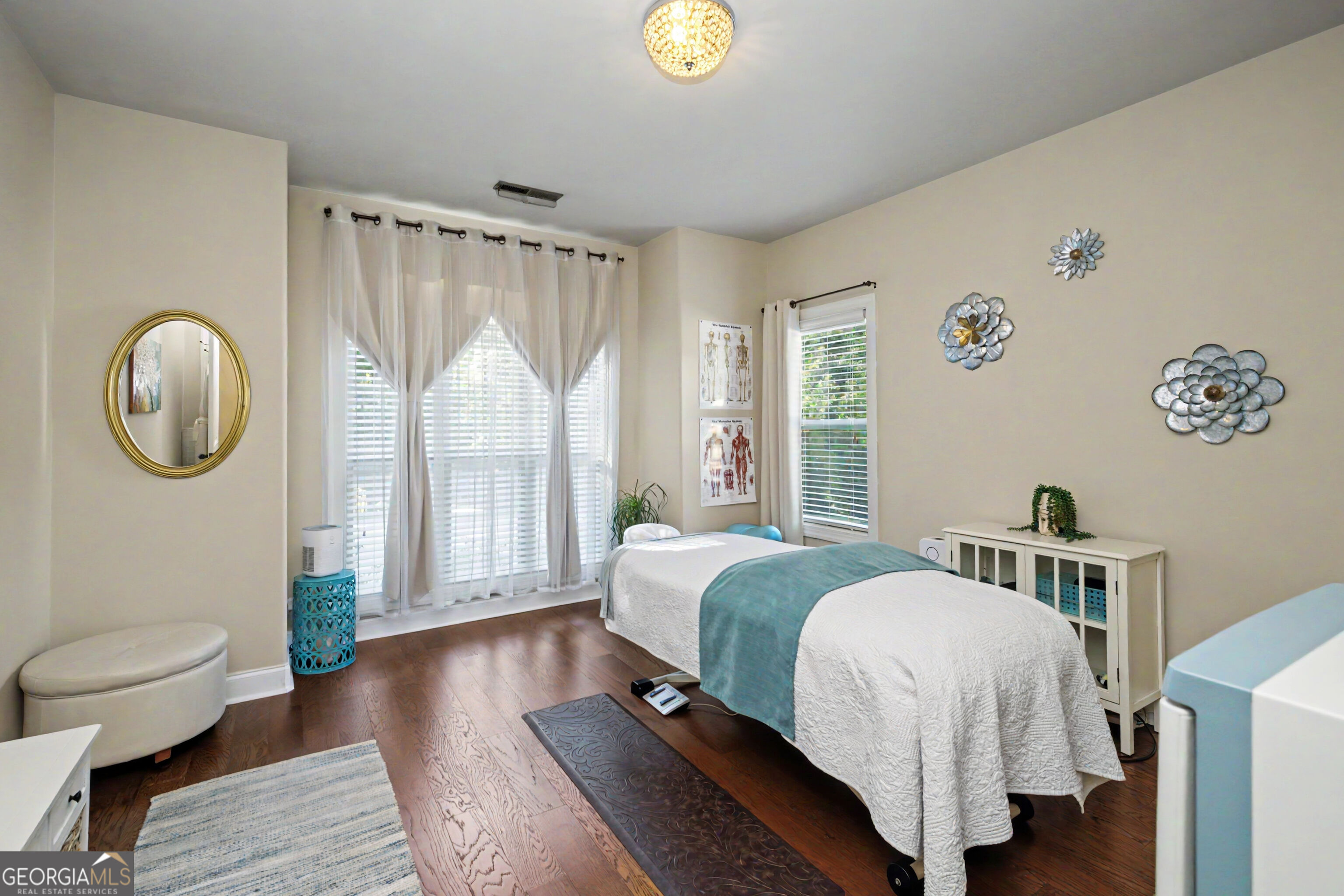 Treatment room with a massage table, anatomical posters, and large curtained windows.