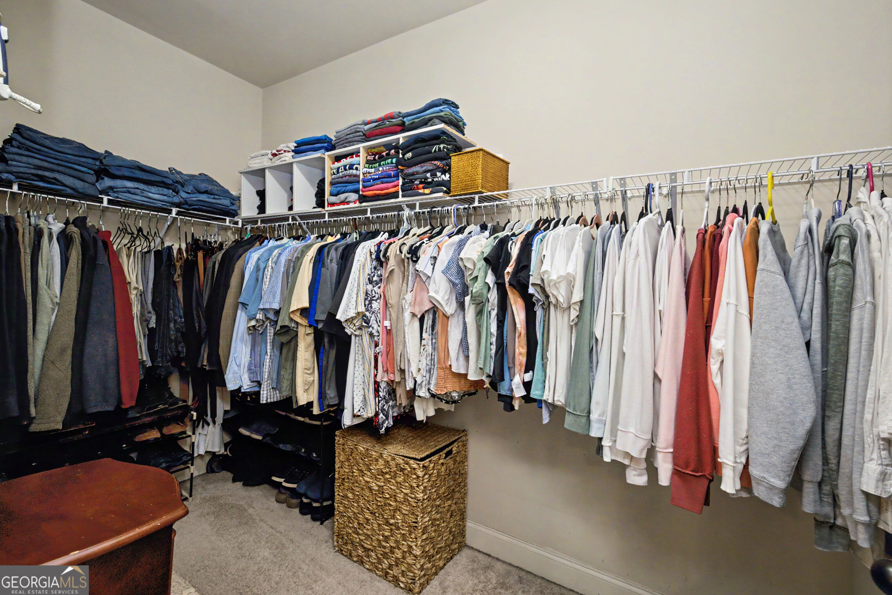 Walk-in closet with long clothing rails, folded clothes on shelves, shoe storage, and woven baskets.