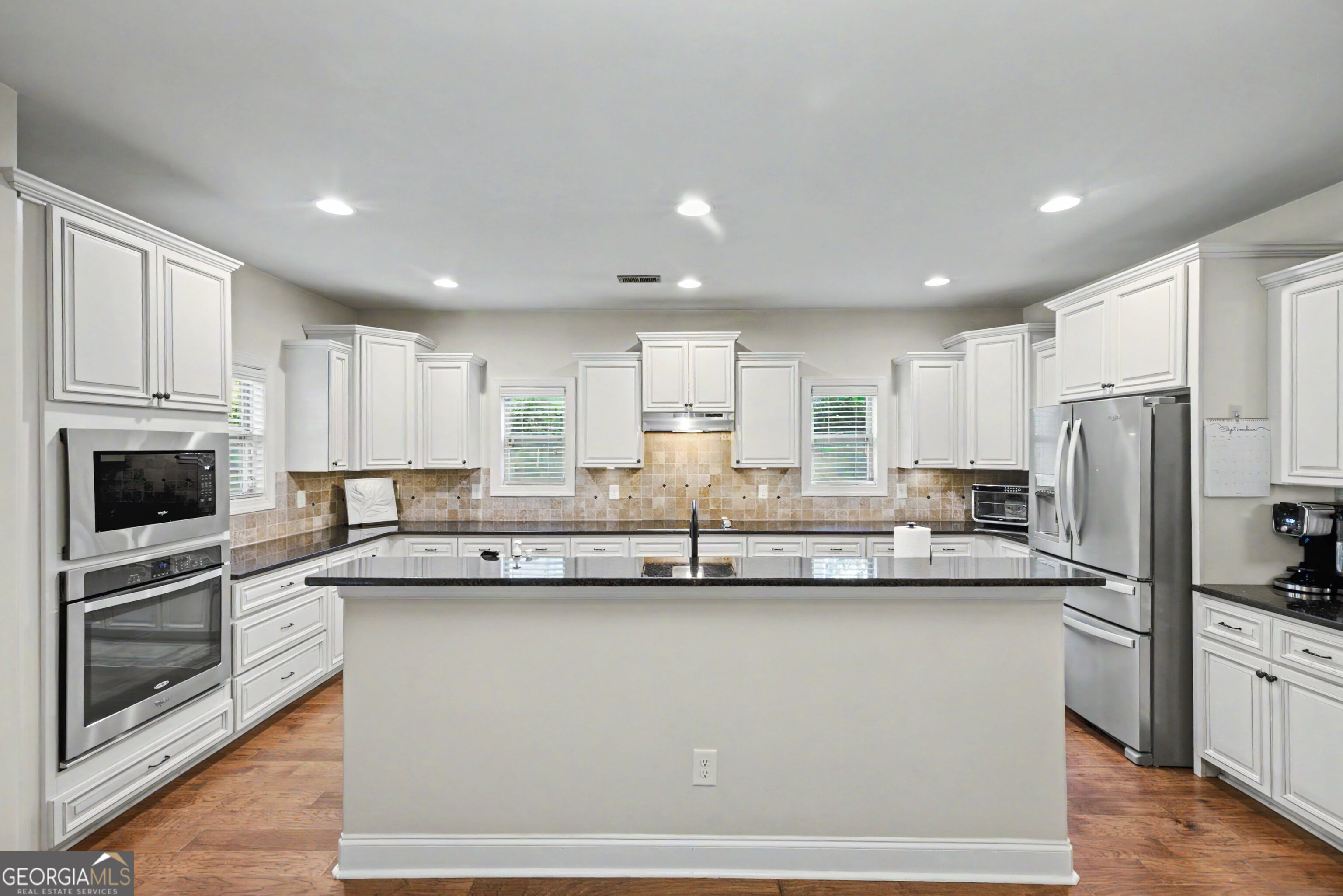 Kitchen with a large island, white cabinets, stainless steel appliances, and a tan tile backsplash.