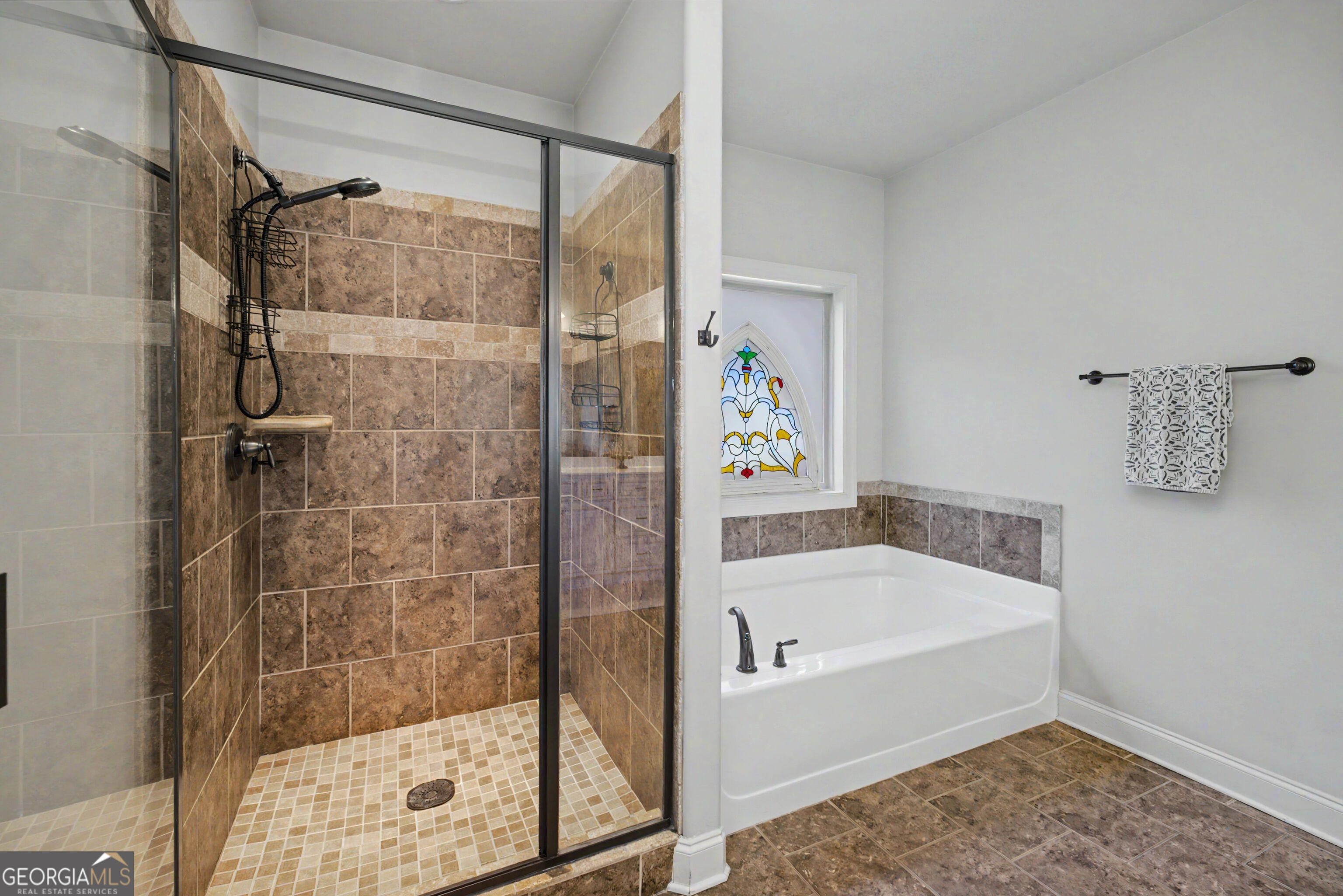 Bathroom with a tiled walk-in shower, white bathtub, and stained-glass window.