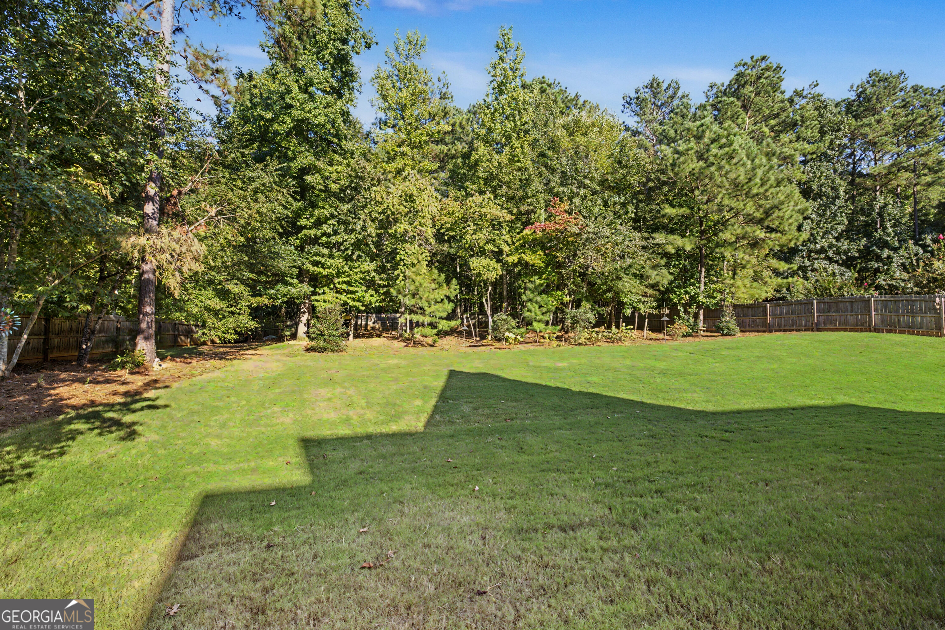 Fenced backyard with a broad lawn, mature trees, and a wooden privacy fence.