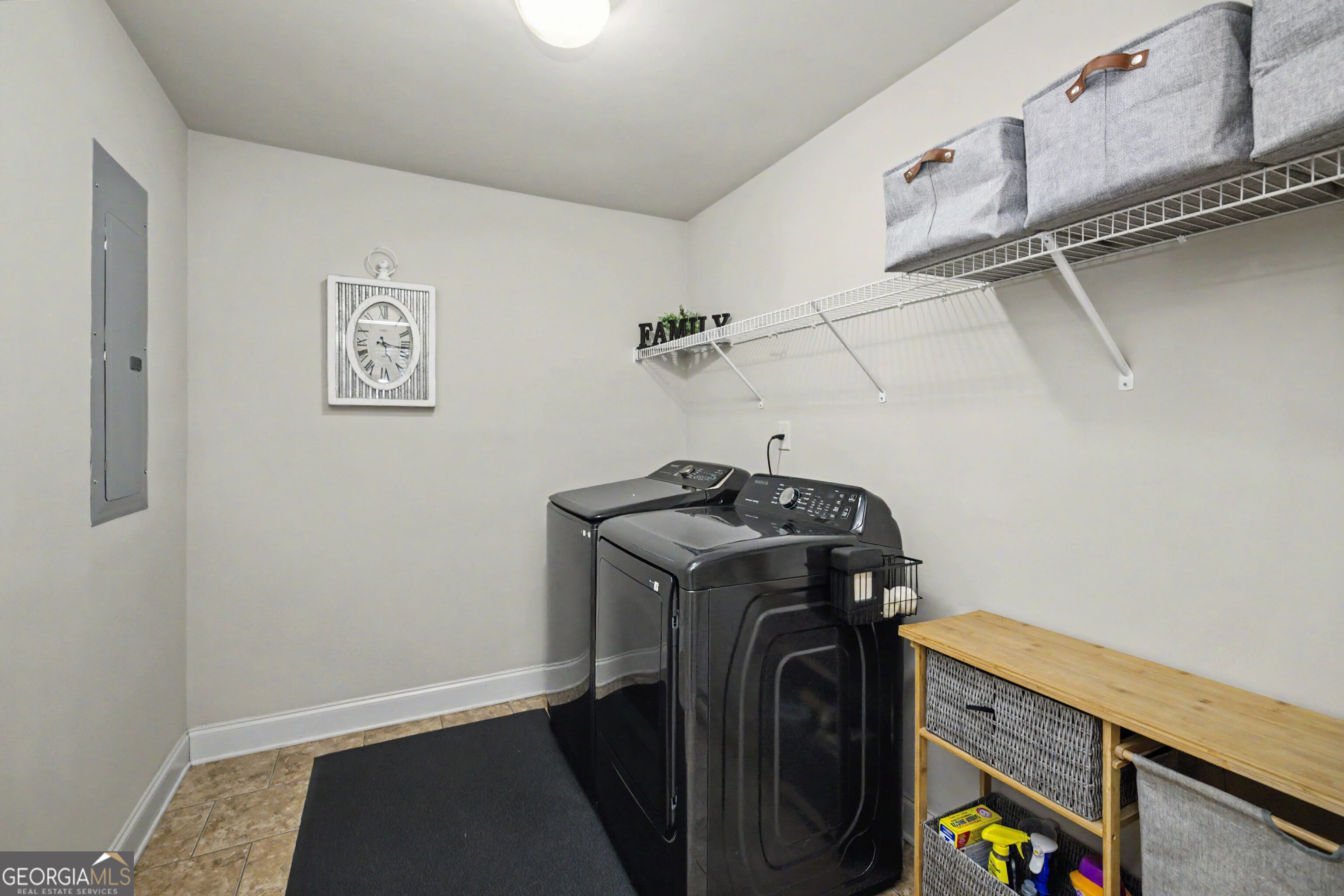 Laundry room with black washer and dryer, overhead wire shelving, and a wooden storage bench.