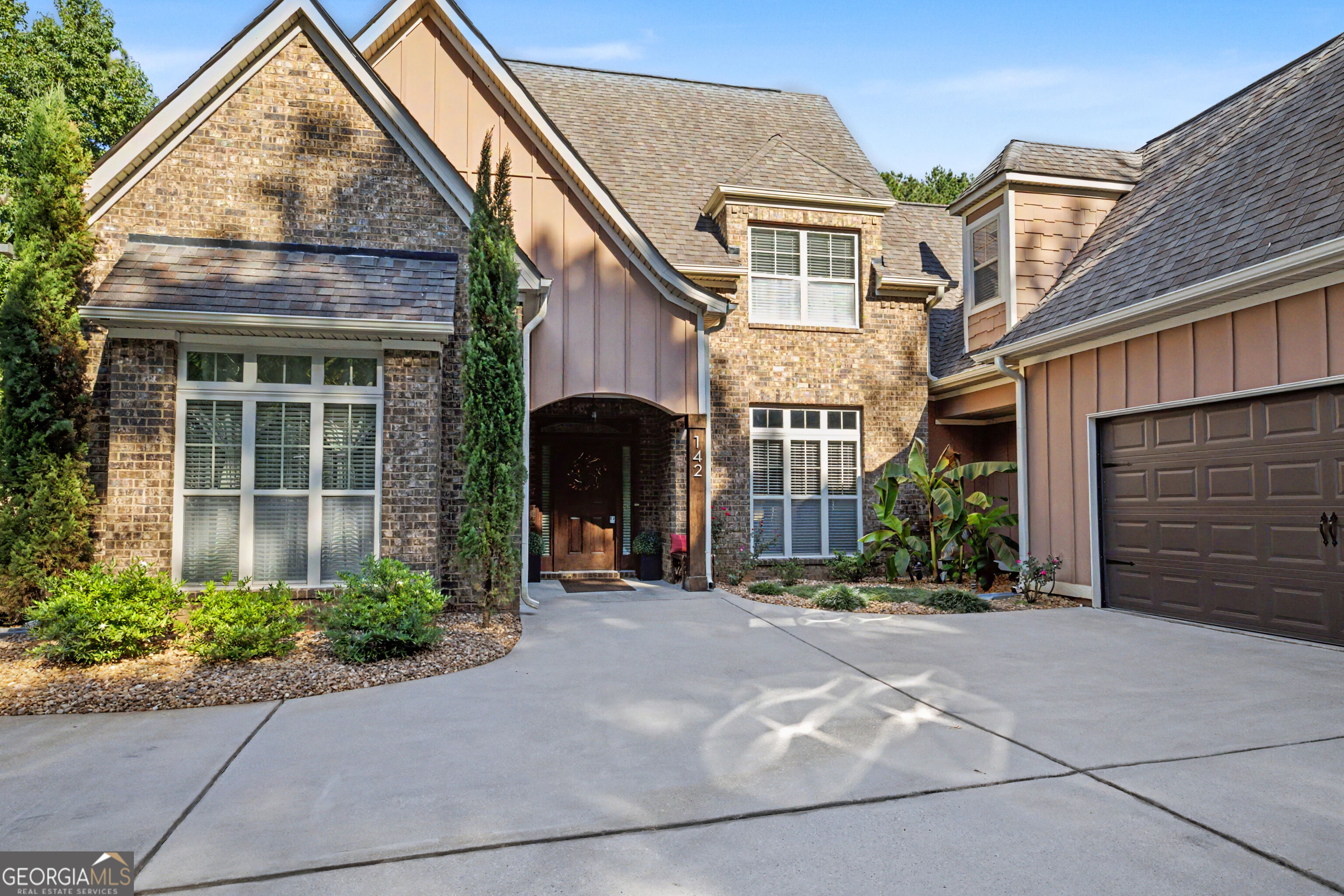 Two-story brick home with a covered entry, attached garage, and wide concrete driveway.