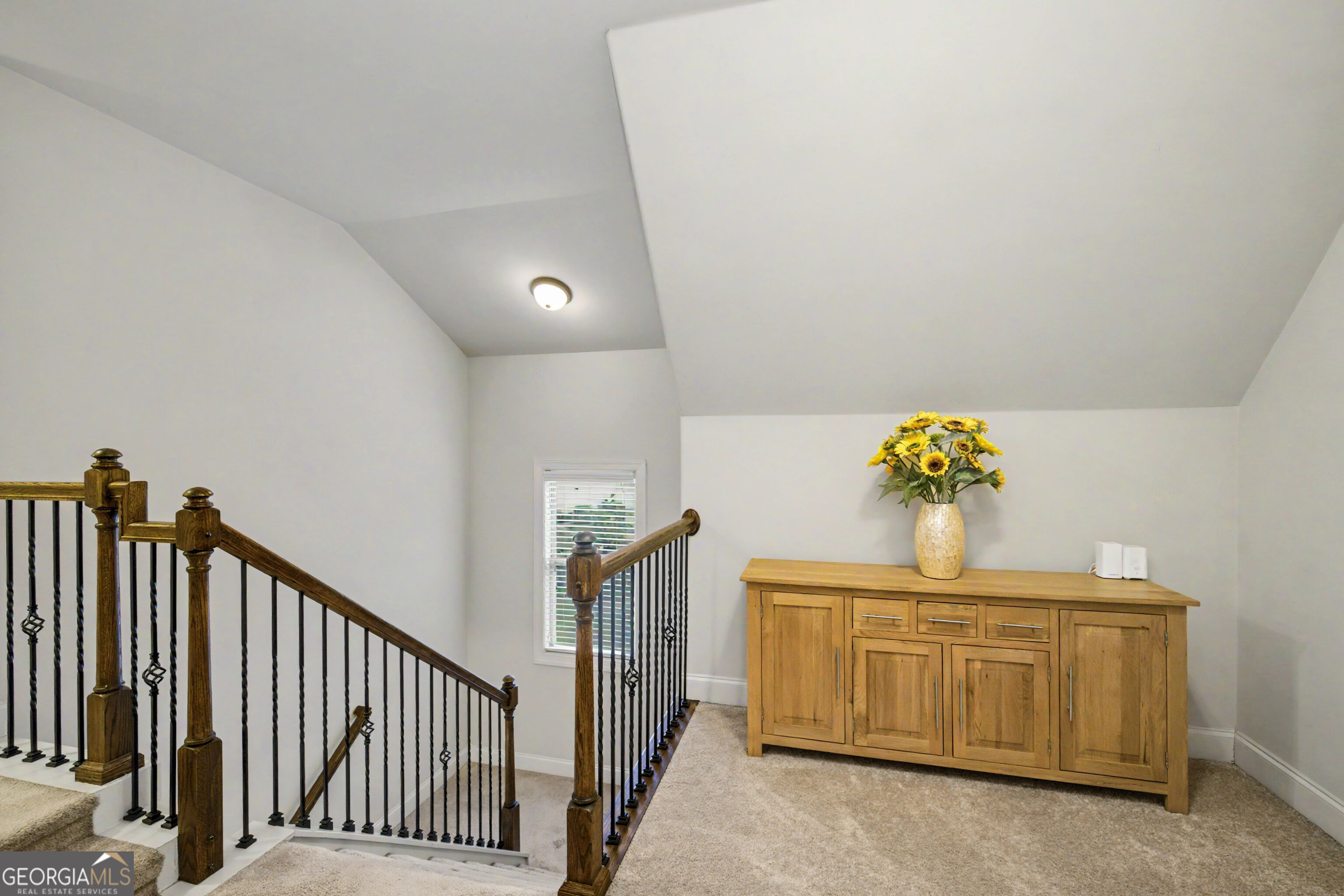 Upstairs landing with a dark wood and iron staircase railing and a wooden console cabinet topped with yellow flowers.
